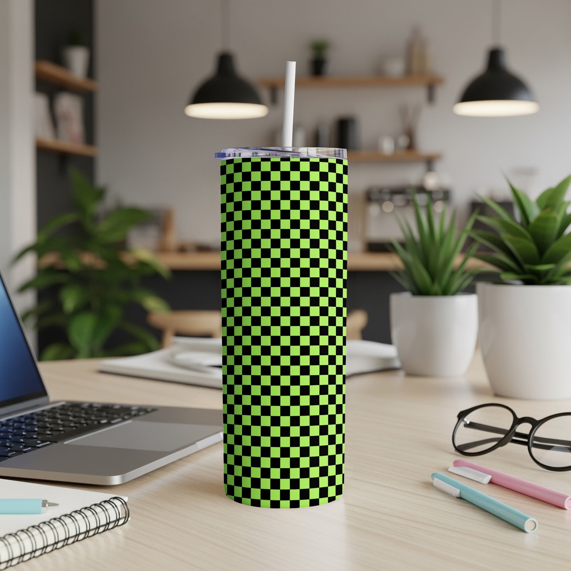 Green and black checkerboard pattern tumbler with white straw on desk.