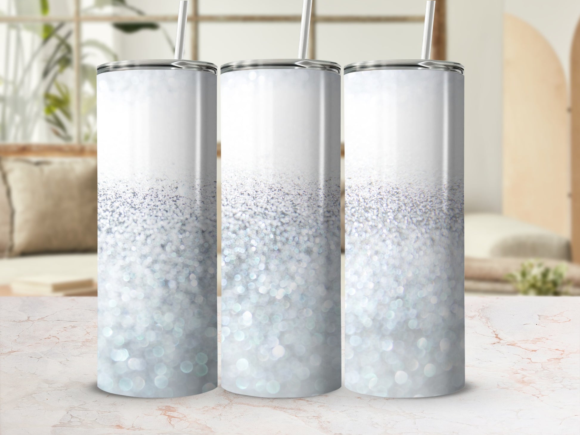 Three silver glitter tumblers with straws on a marble surface.