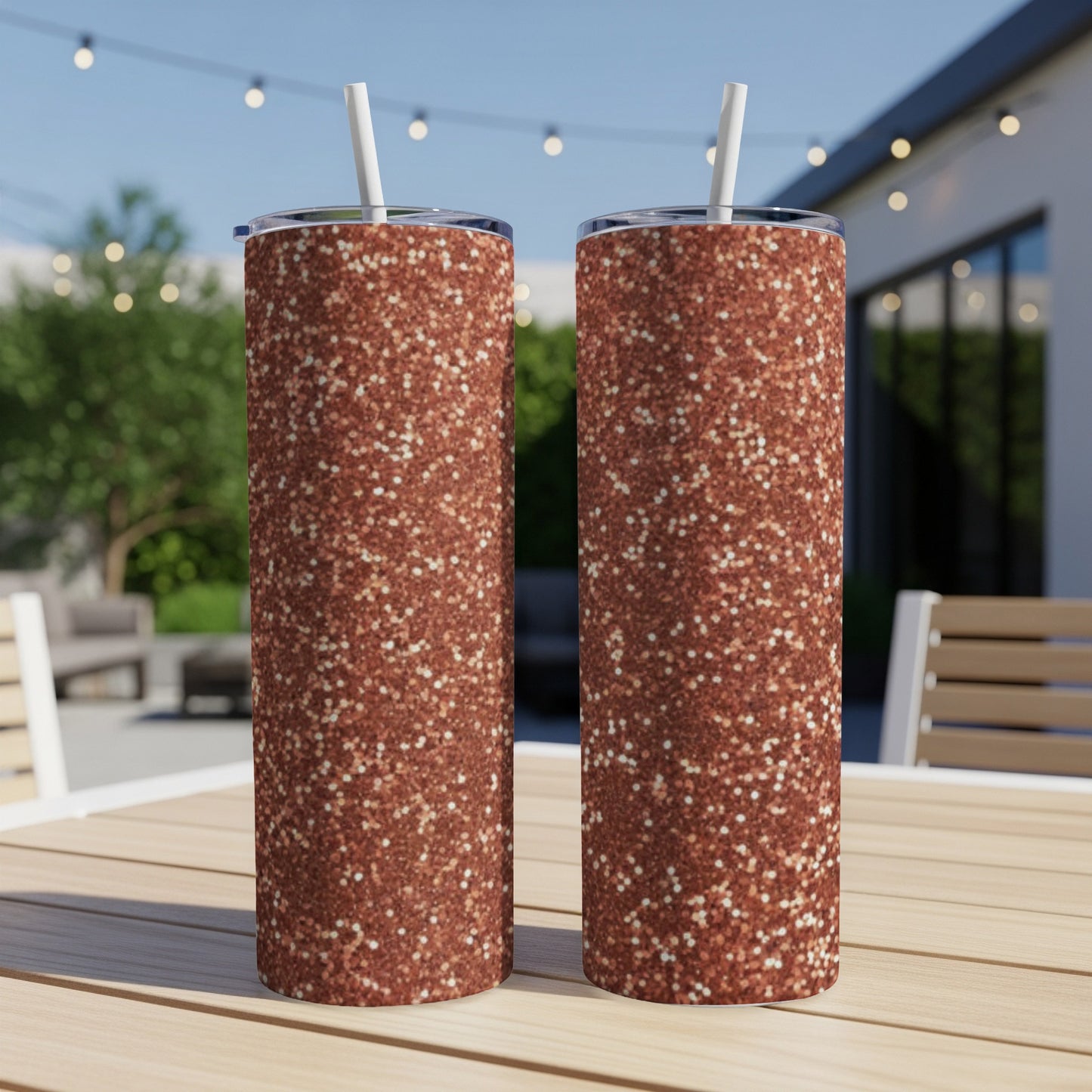 Two rose gold glitter tumblers with straws on a wooden table.