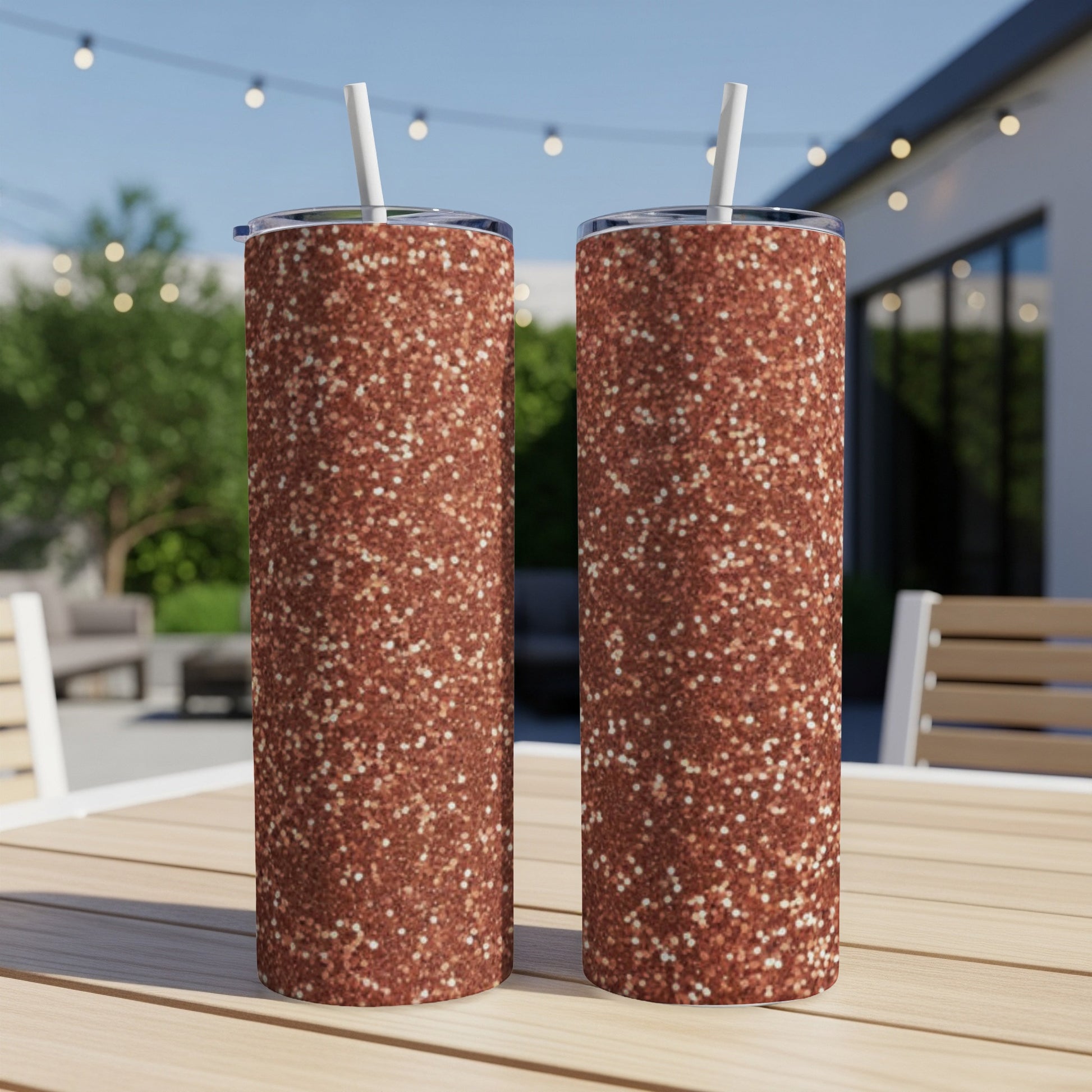 Two rose gold glitter tumblers with straws on a wooden table.