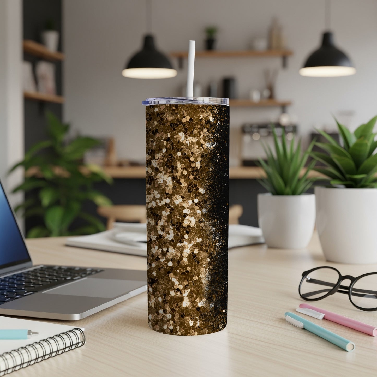 Gold and black glitter tumbler with a white straw on a wooden desk.