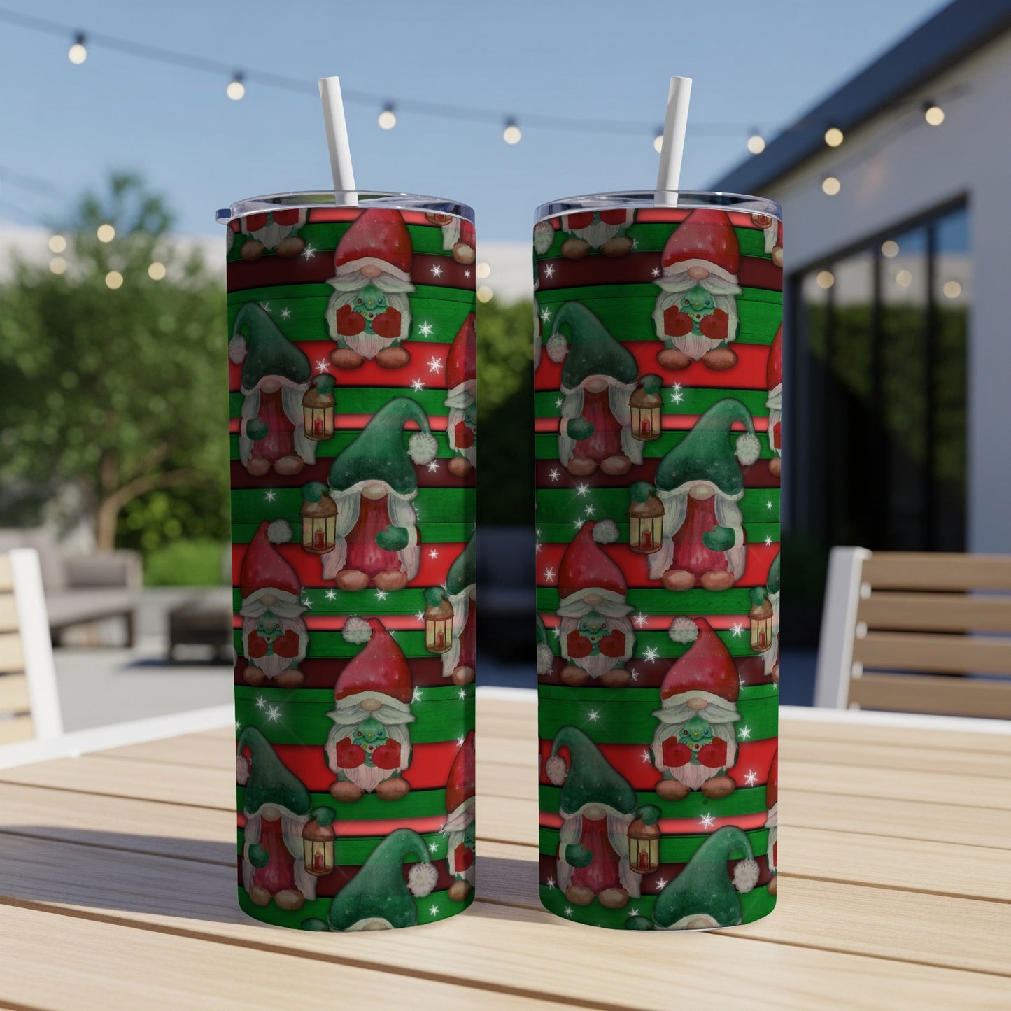 Two tumblers with a gnome and lantern pattern on a wooden table outdoors.