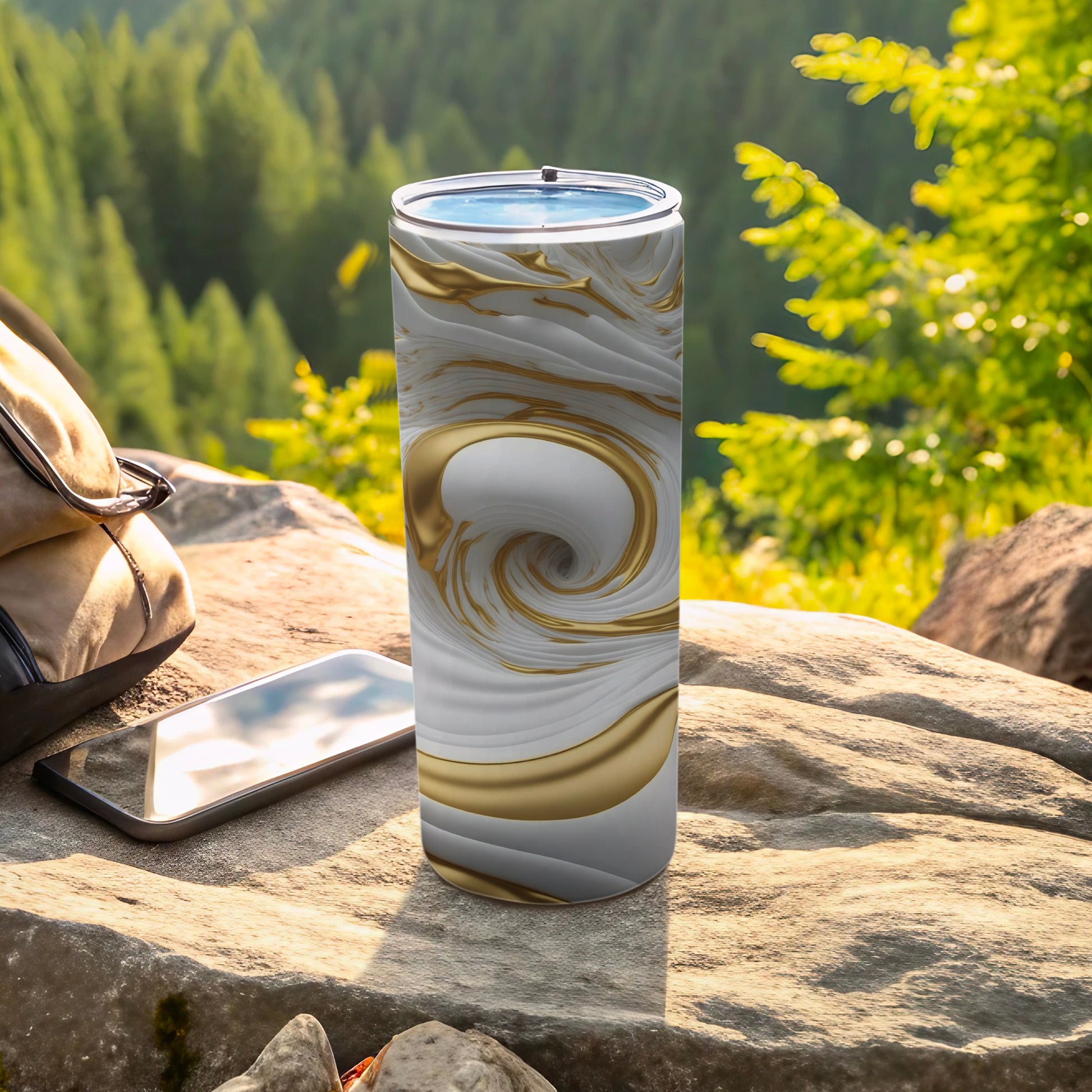 White and gold swirled tumbler on rock with phone and backpack.
