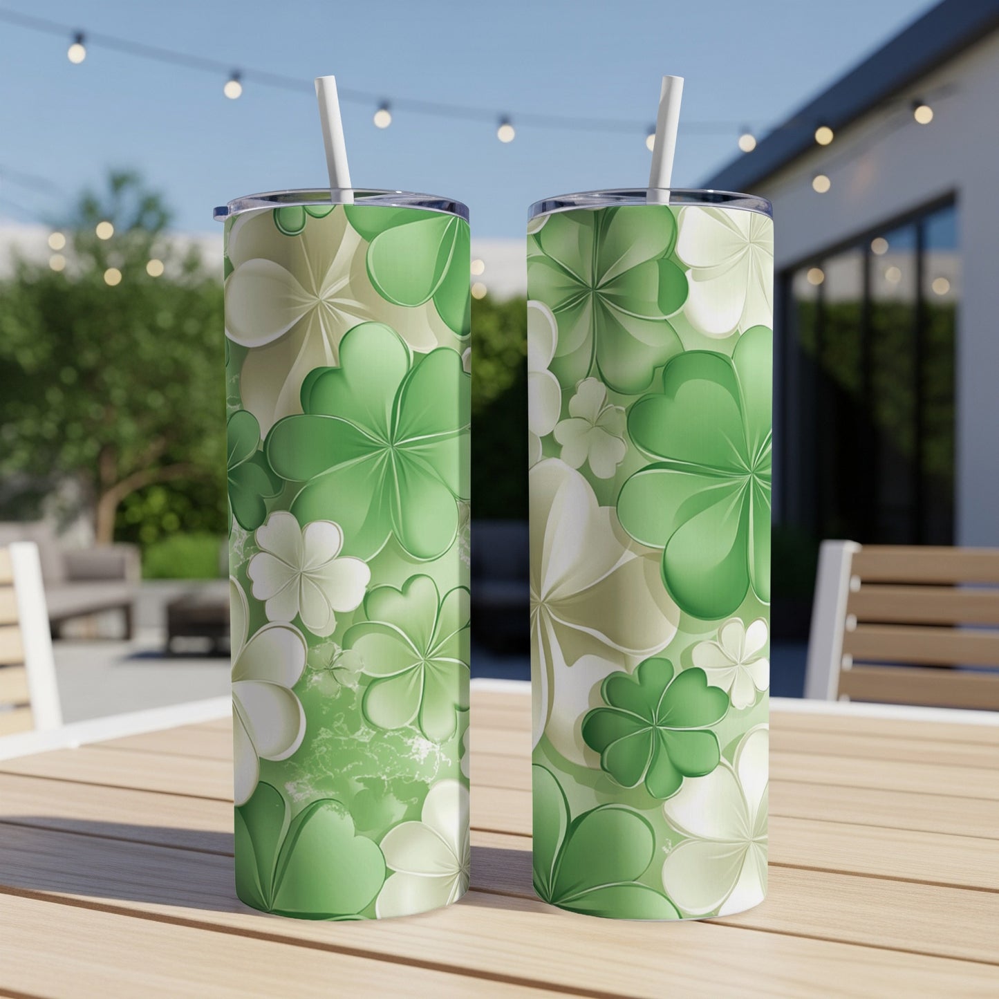 Two green floral tumblers with straws sit on a wooden table outdoors.