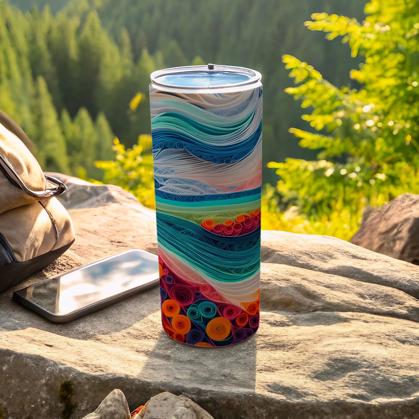 Tumbler with colorful abstract wave pattern resting on rocks outdoors.