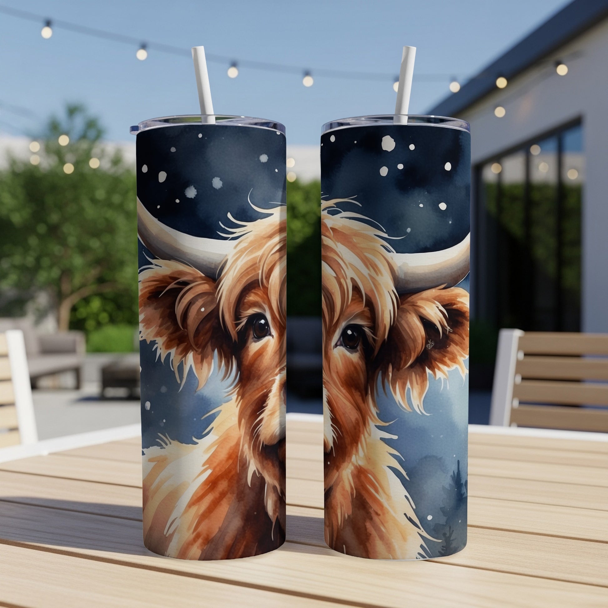 Two tumblers with a watercolor highland cow face design sit on a table.