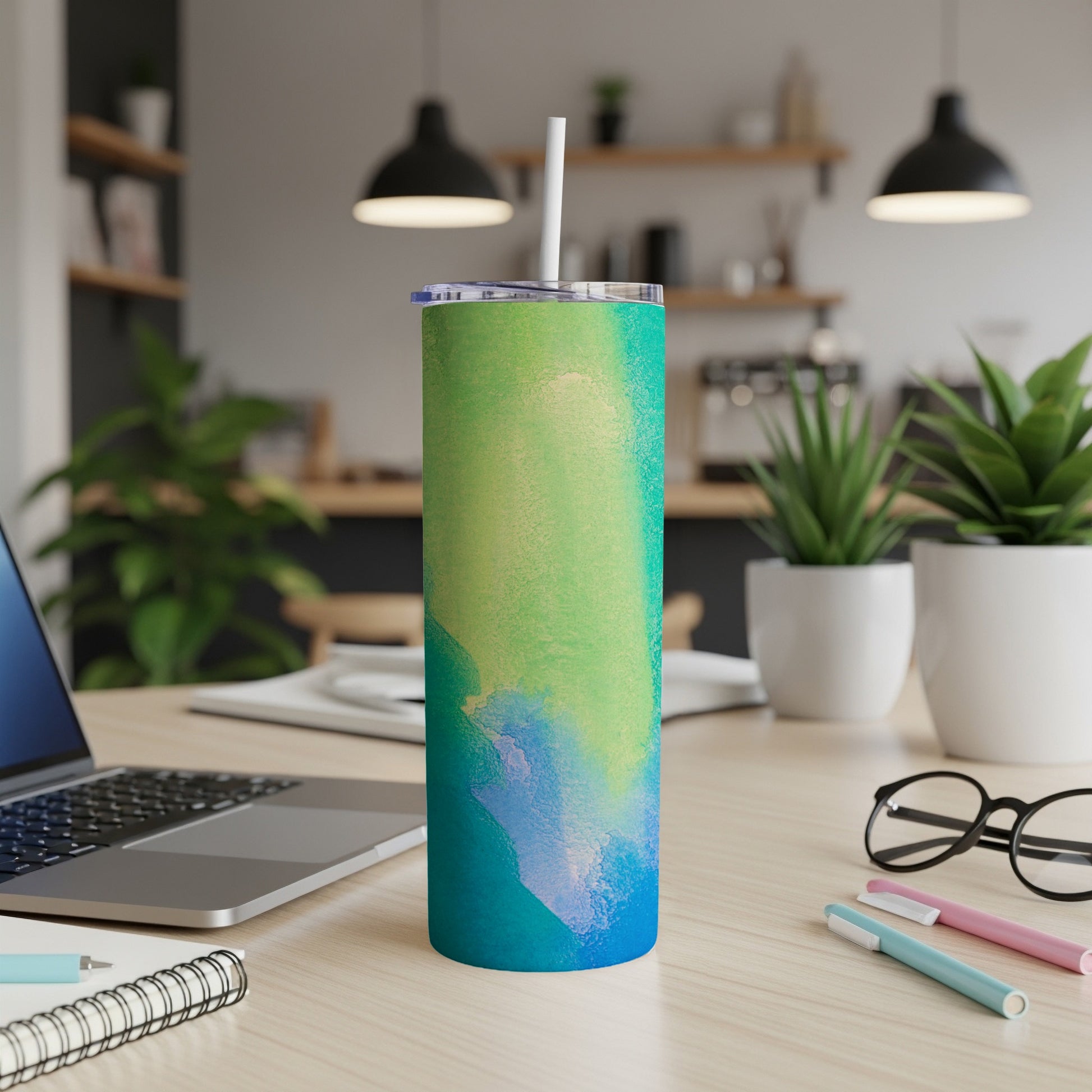 Abstract watercolor tumbler with blue, green, and yellow hues on a desk.