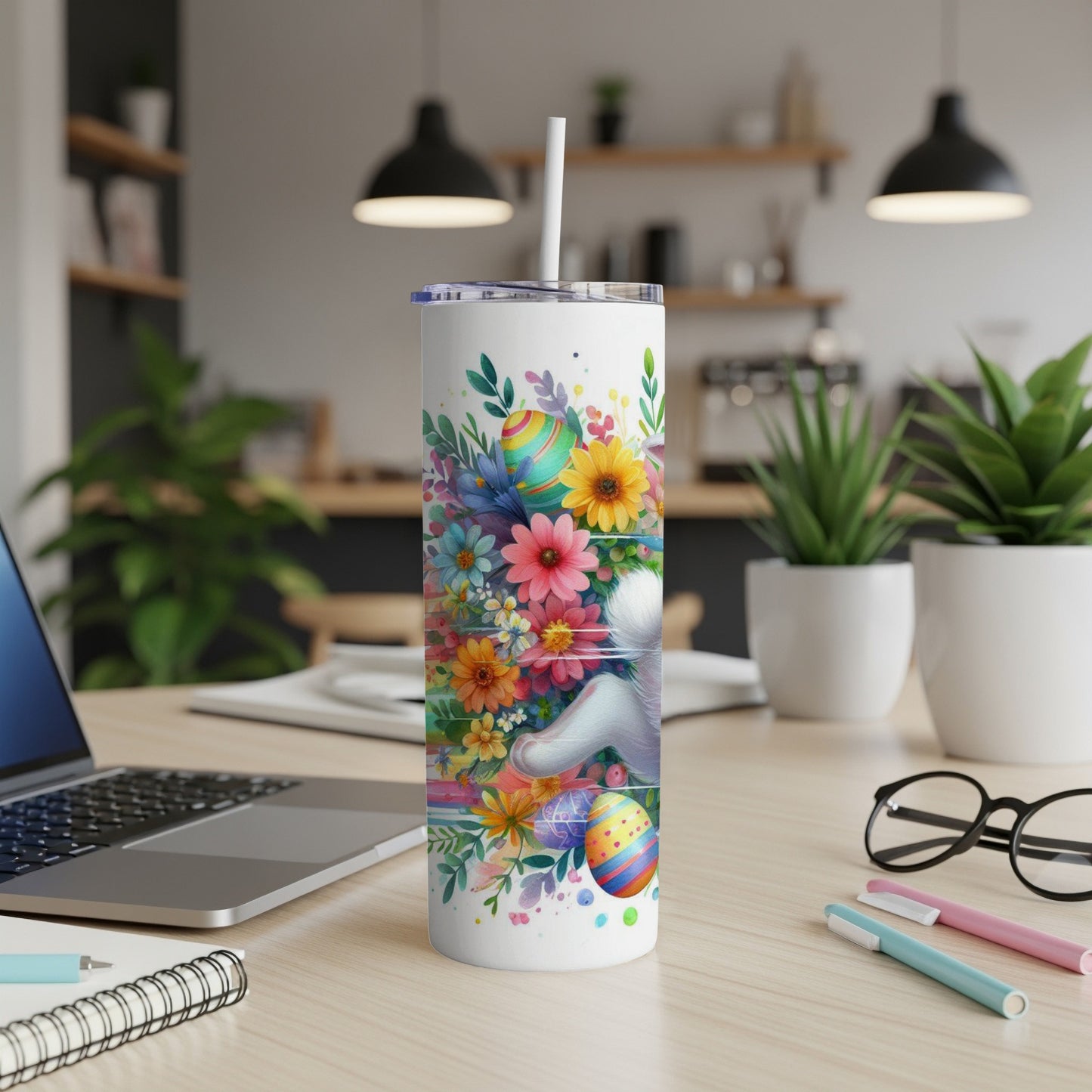 White tumbler with colorful Easter eggs and flowers, laptop on desk.