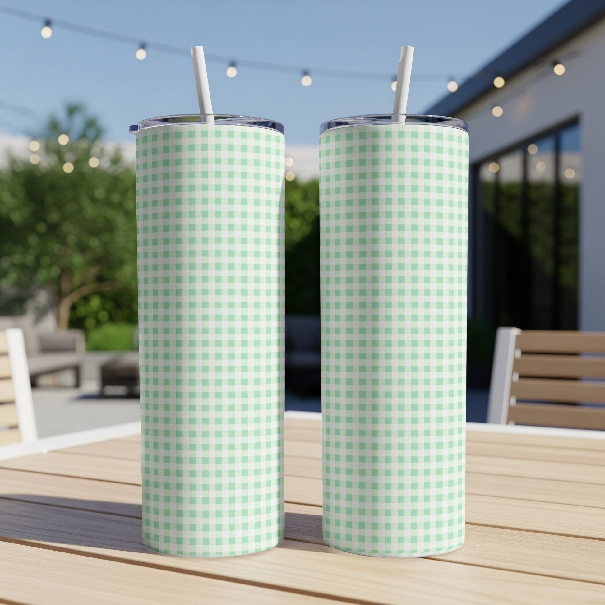 Two mint green and white checkered tumblers with straws on a wooden table.