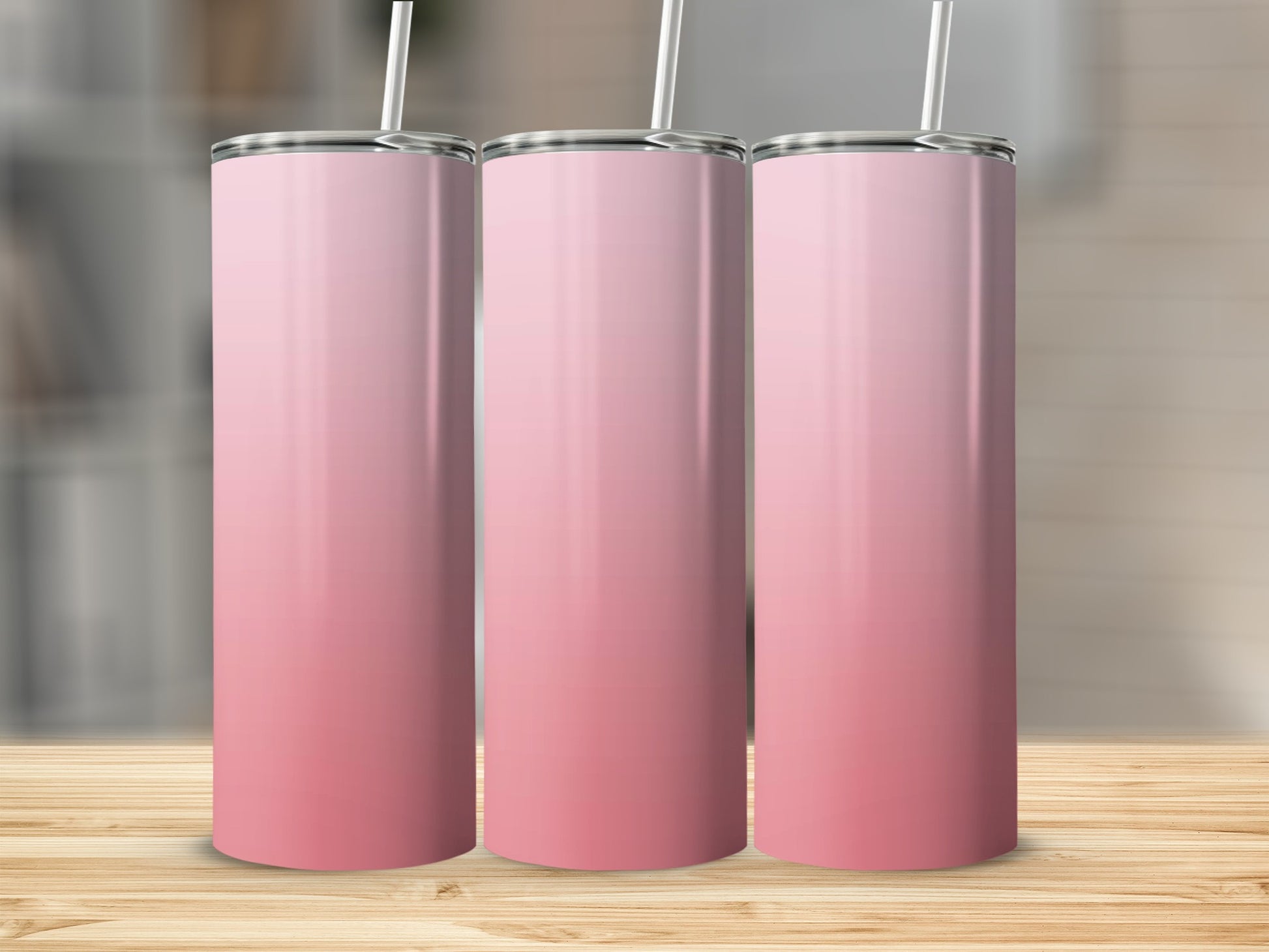 Three pink gradient tumblers with straws on a wooden surface.