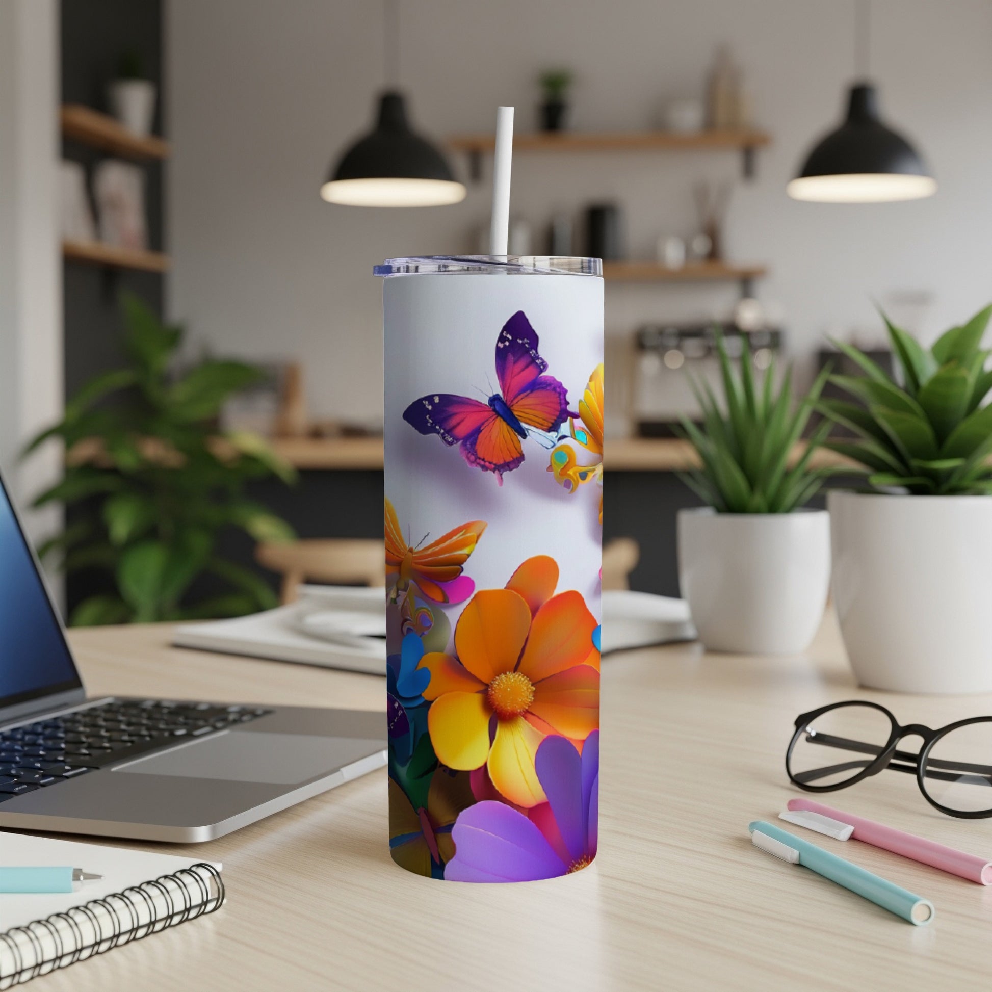 Tall tumbler with colorful flowers and butterflies, on a desk.