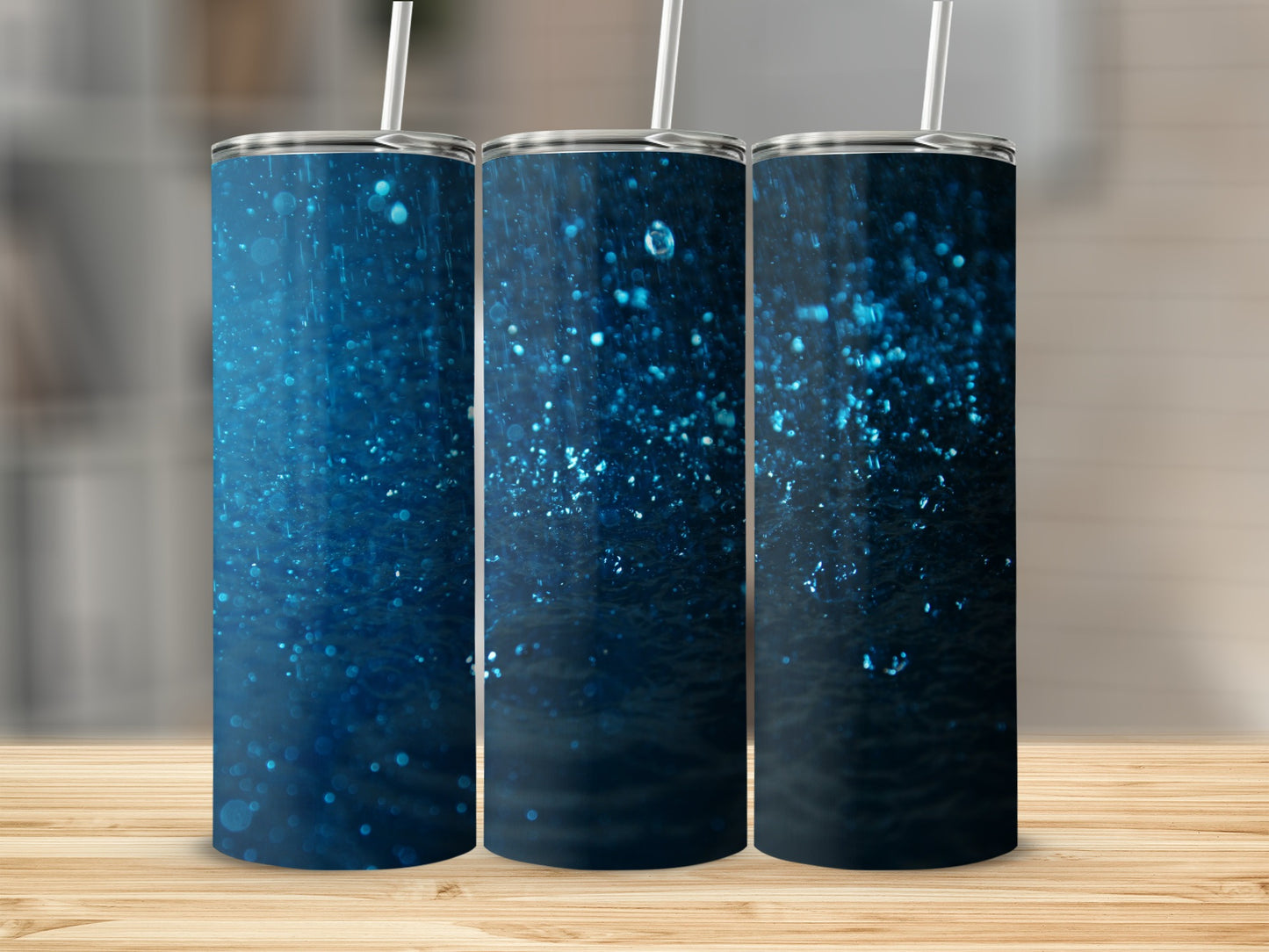 Three blue glitter tumblers with straws on a wooden surface.