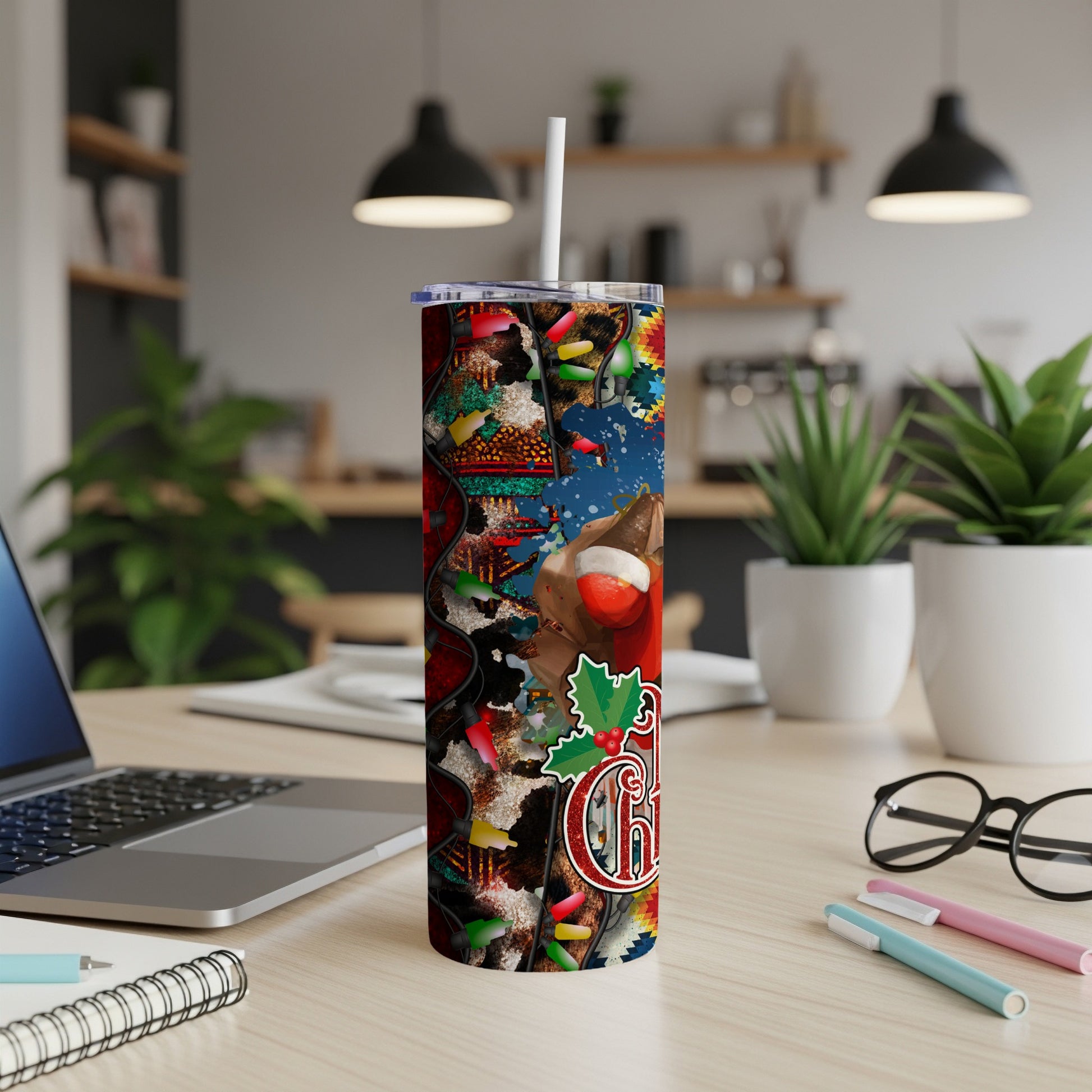Tall tumbler with Christmas pattern, a mug, and laptop on a desk.