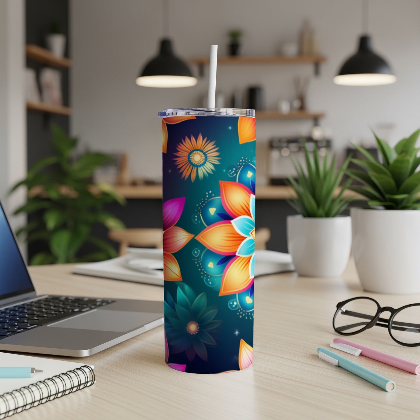 Tall tumbler with a vibrant floral pattern on a desk with a laptop and pens.