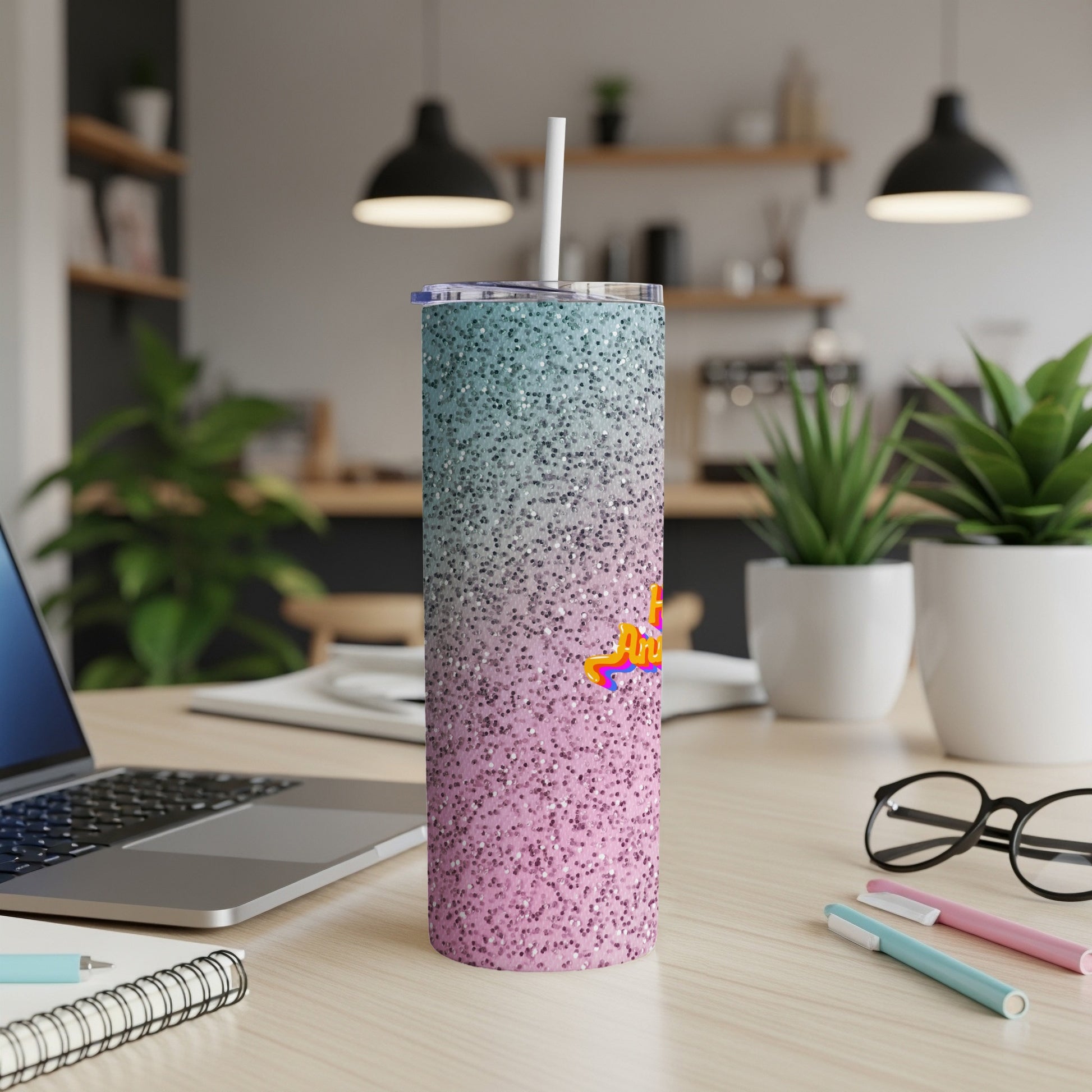 Glittery tumbler with "Awesome" text on a desk with a laptop and pens.