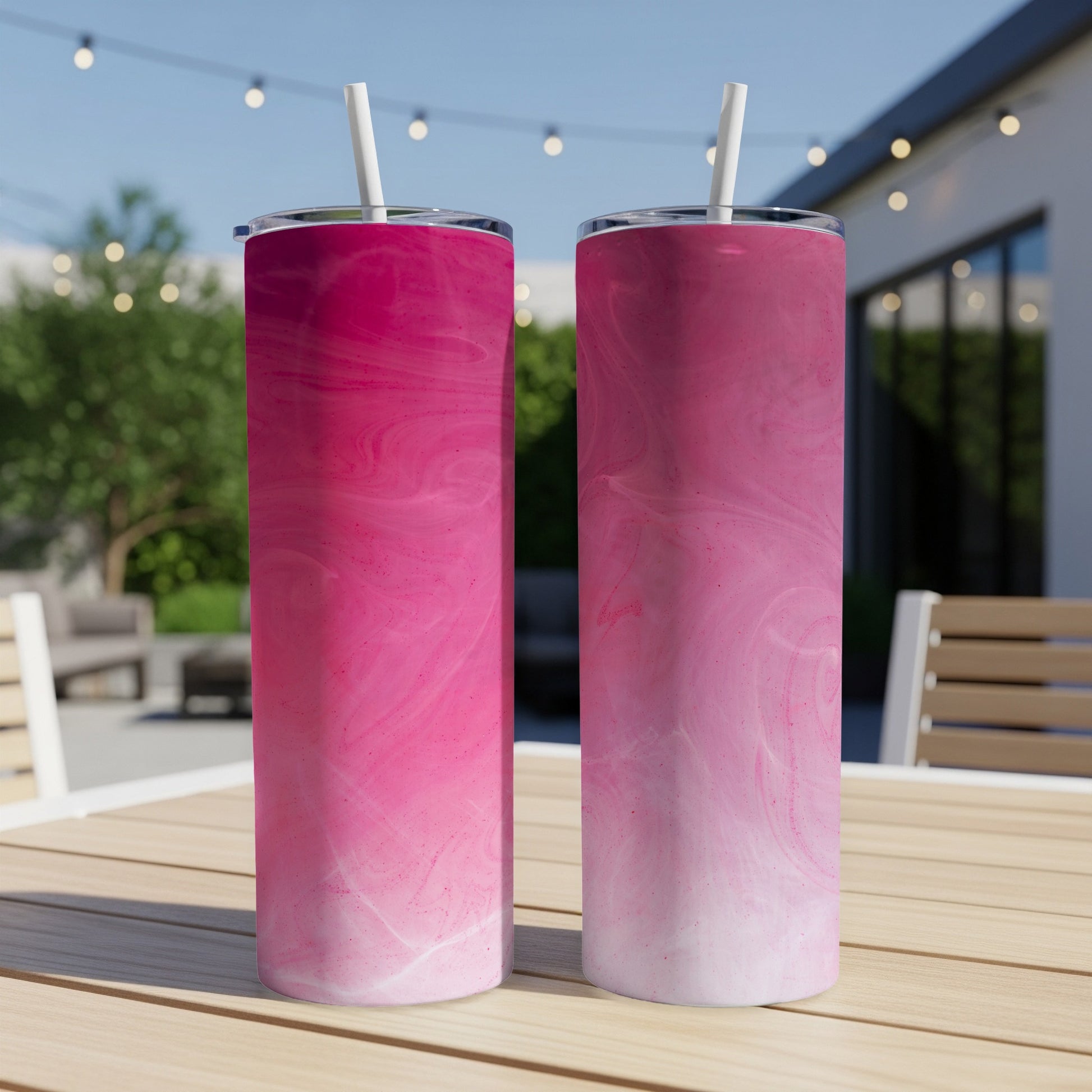 Two pink marbled tumblers with straws on a table outdoors.