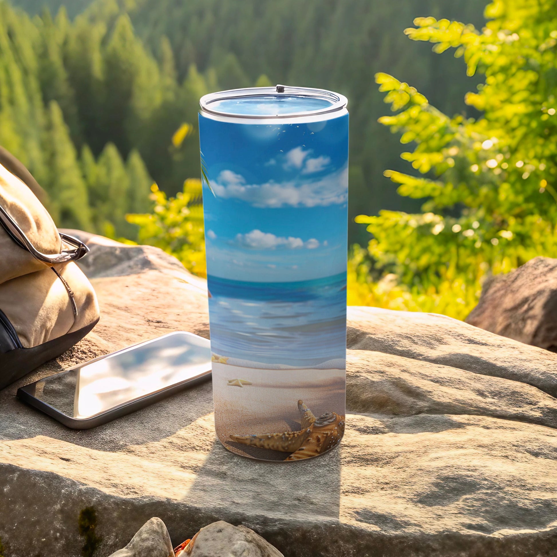Beach scene tumbler with starfish on sand, next to phone and bag.