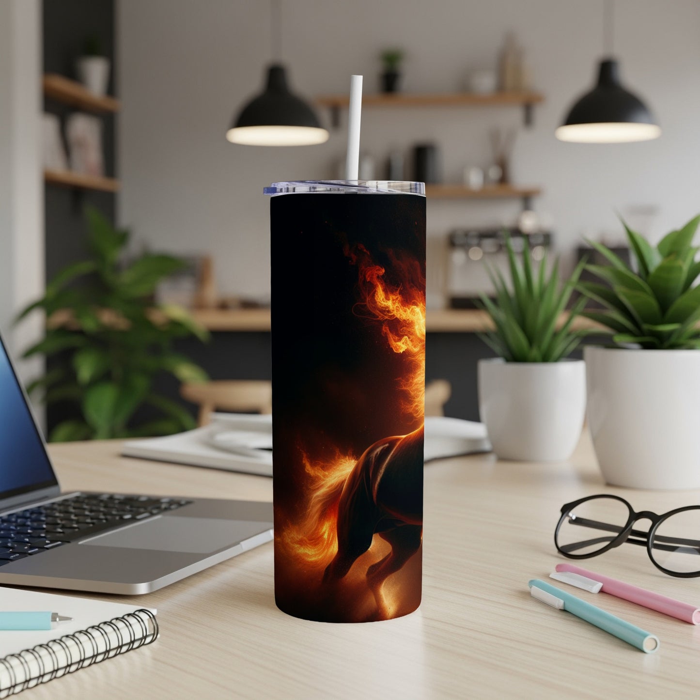 Tumbler with a fiery horse design on a desk with a laptop and pens.