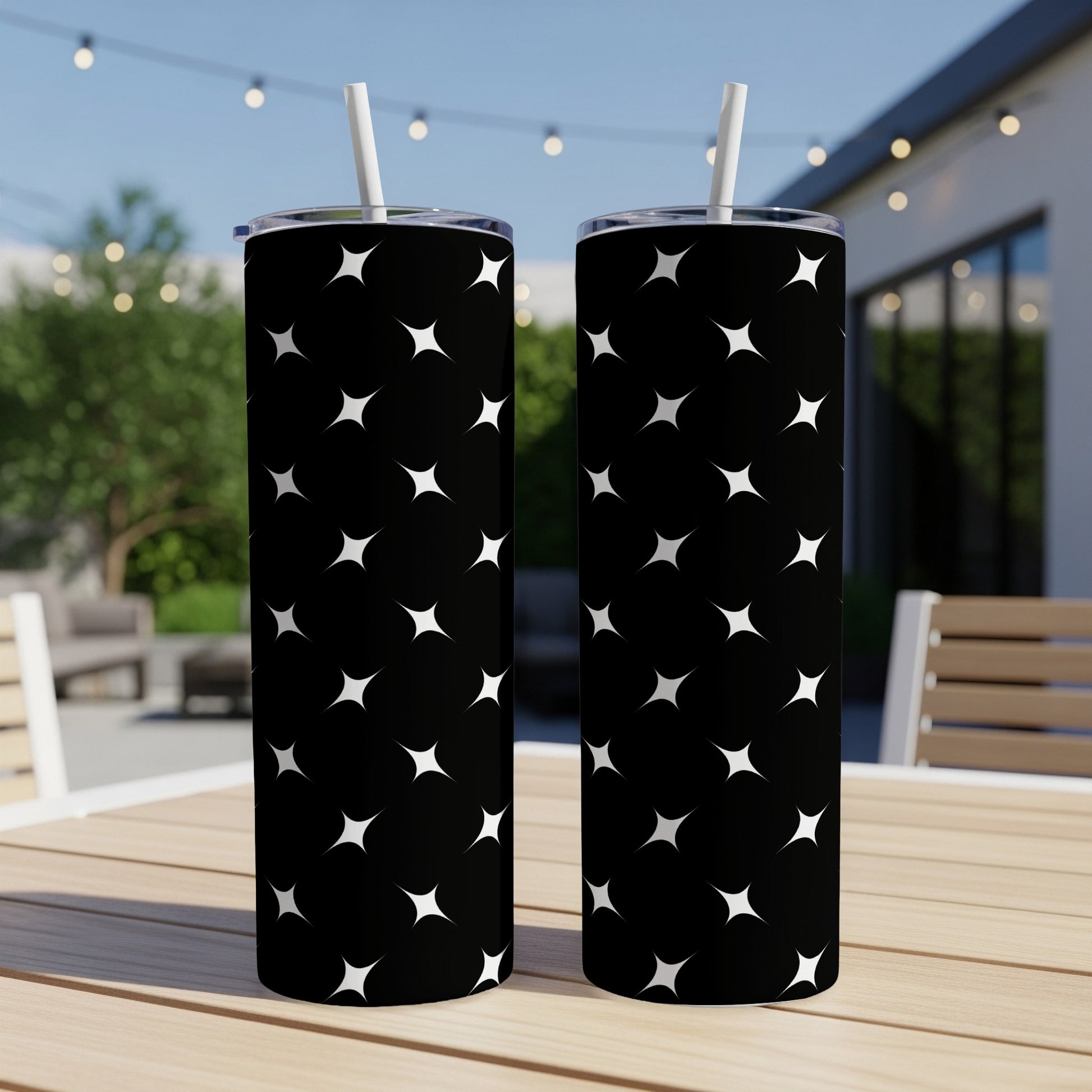 Two black tumblers with white star pattern and straws on a wooden table.