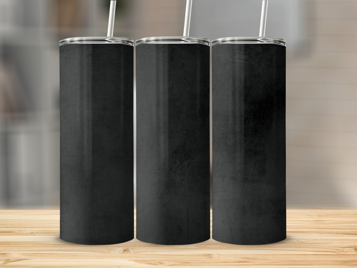 Three blank black tumblers with straws stand on a wooden surface.
