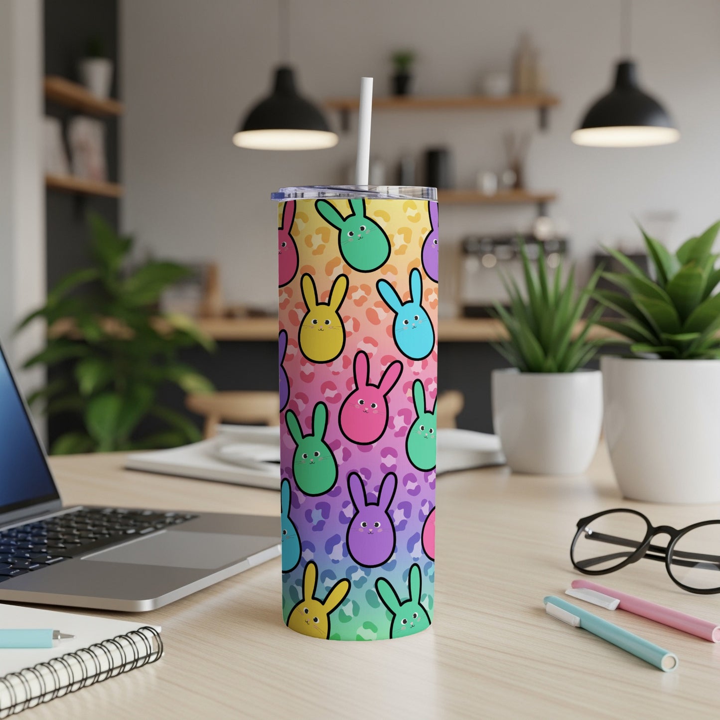 Colorful bunny pattern on a skinny tumbler with a straw on a desk.