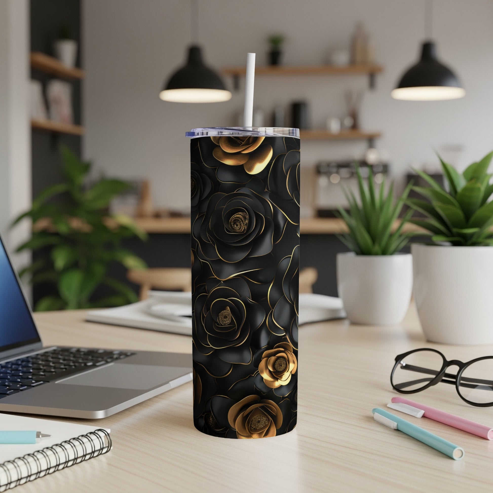 Black tumbler with gold roses, straw, on a desk with laptop and supplies.