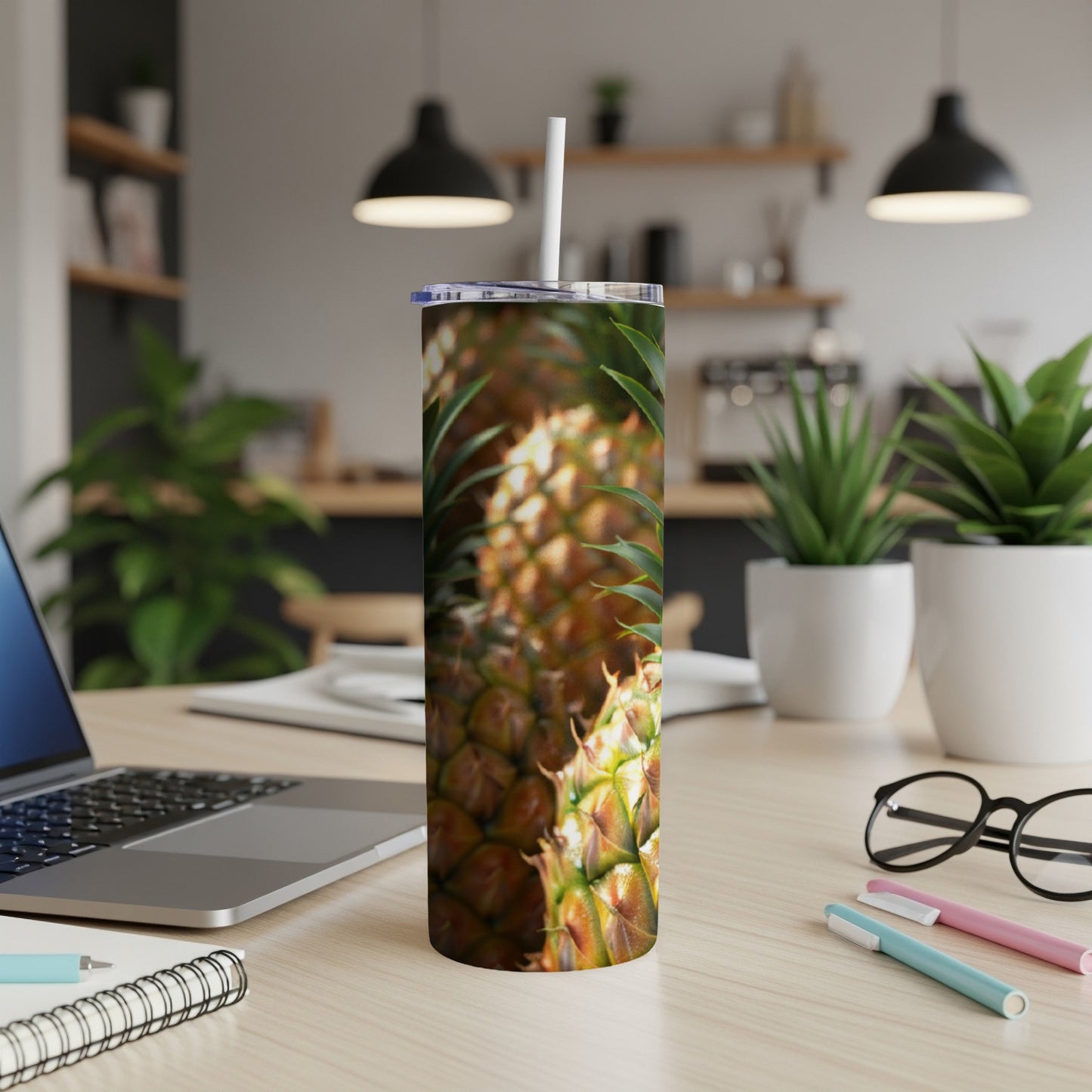 Pineapple pattern on a white tumbler with a straw, on a desk.