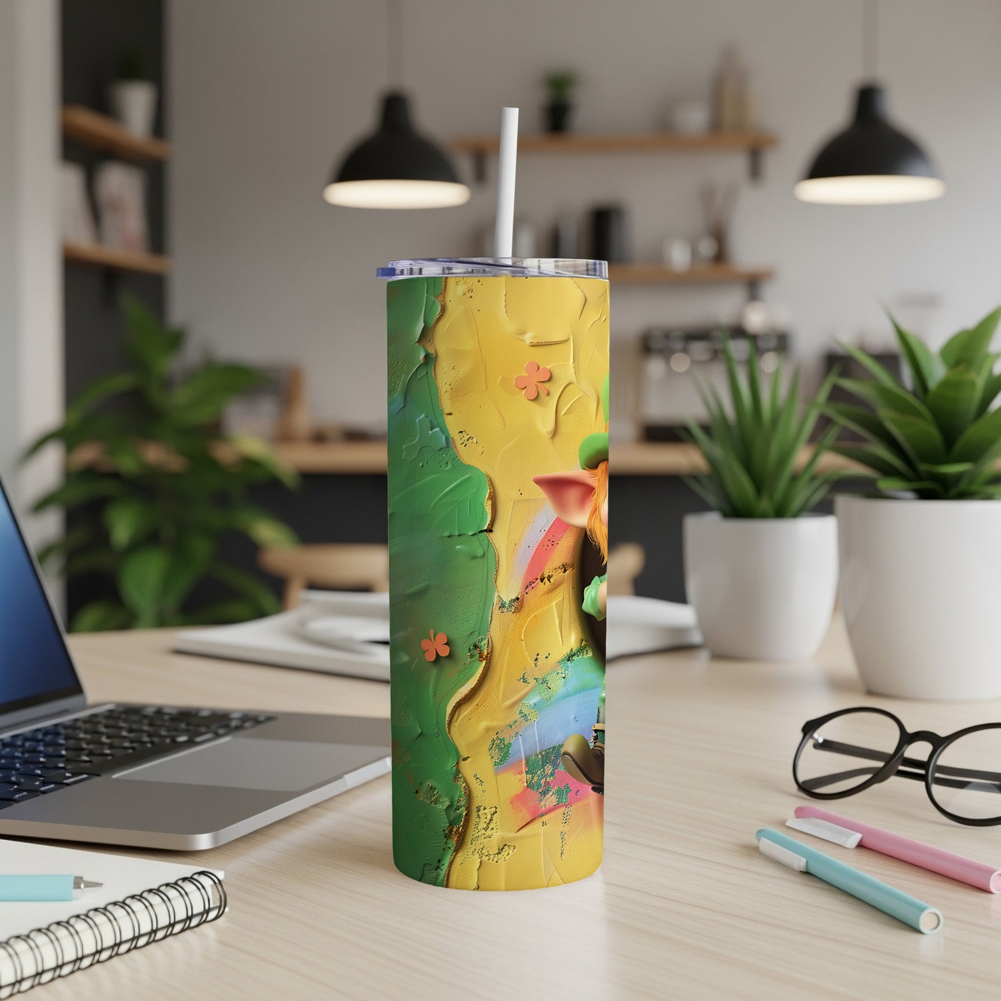 Green and yellow abstract art tumbler with straw, on a desk.