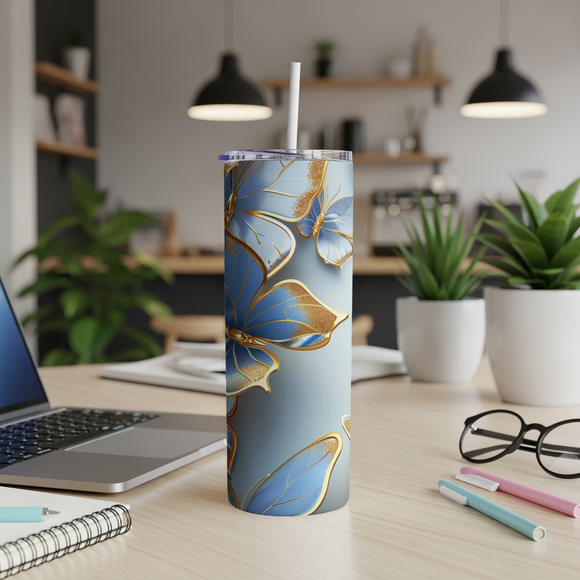 Blue and gold butterfly patterned tumbler with straw on a desk.