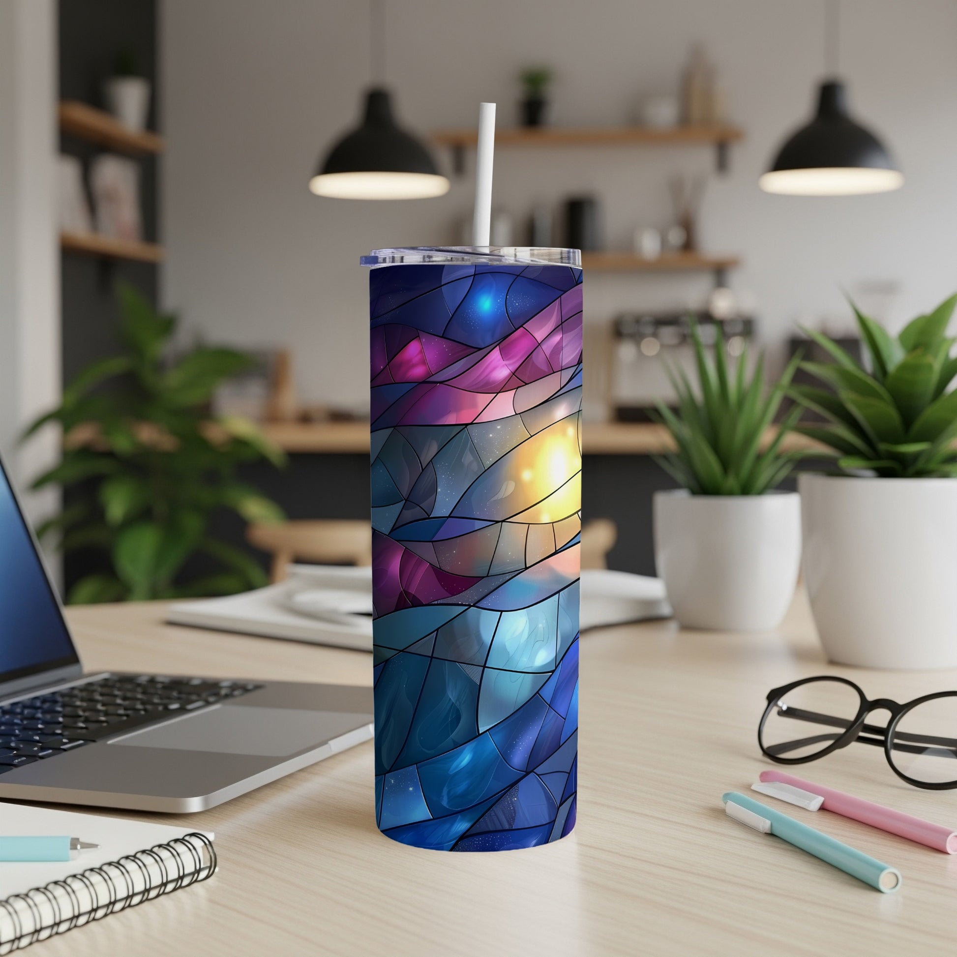 Tumbler with stained glass galaxy design and straw, on a desk.