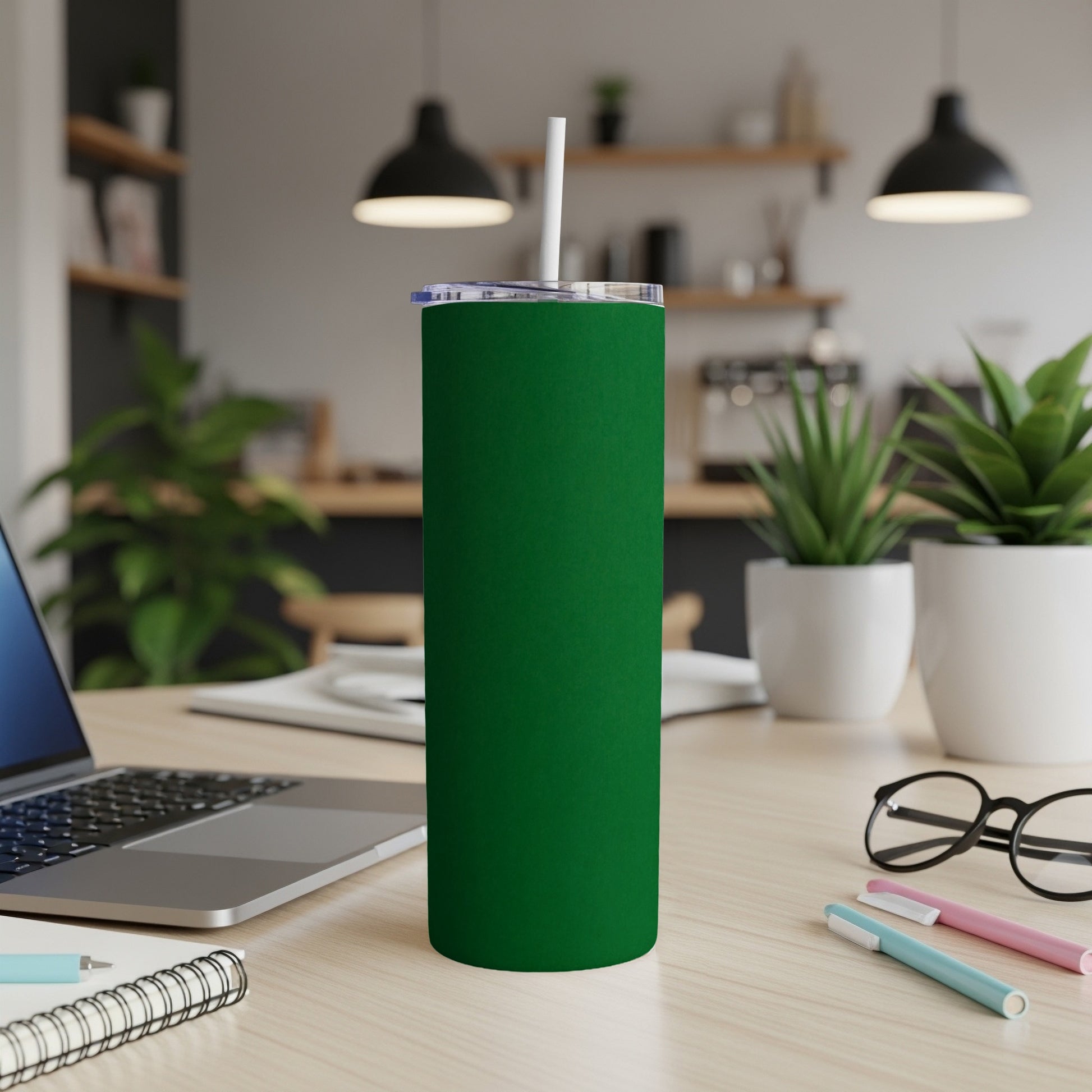 Green tumbler with straw on a desk next to a laptop.