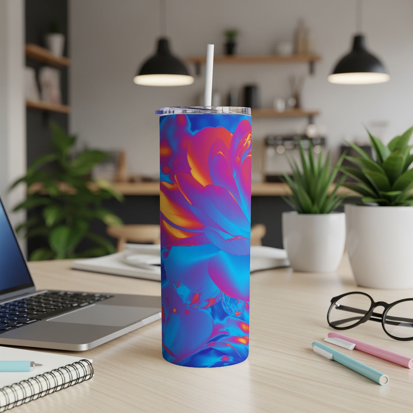 Tumbler with colorful floral abstract design, on a desk with laptop and pens.