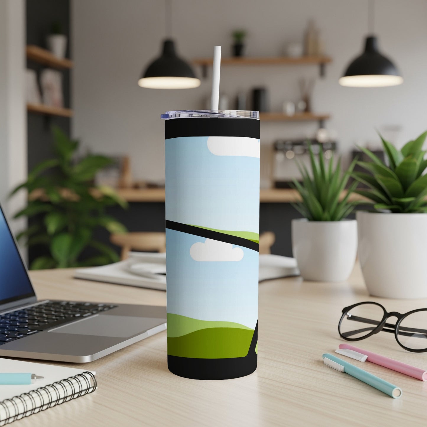 Black tumbler with a landscape design and white straw on a desk.