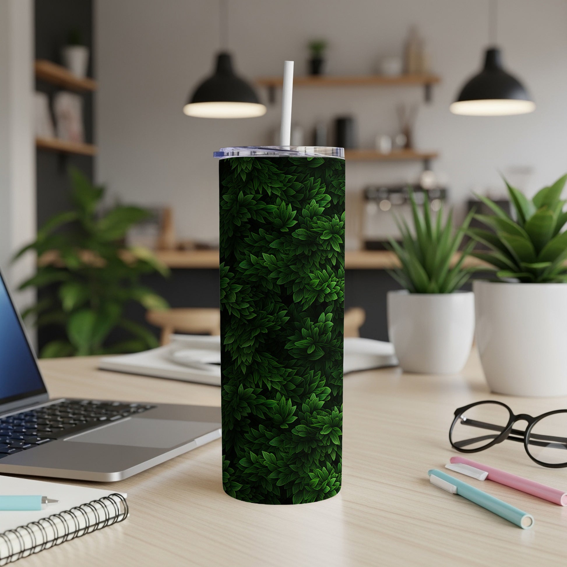 Dark green leaves pattern on a tall tumbler with a straw, on a desk.