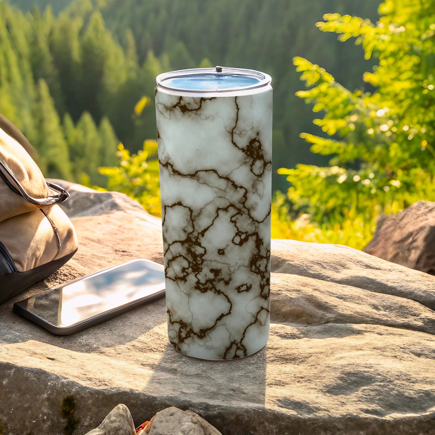 Marble pattern tumbler on a rock with a phone and backpack outdoors.
