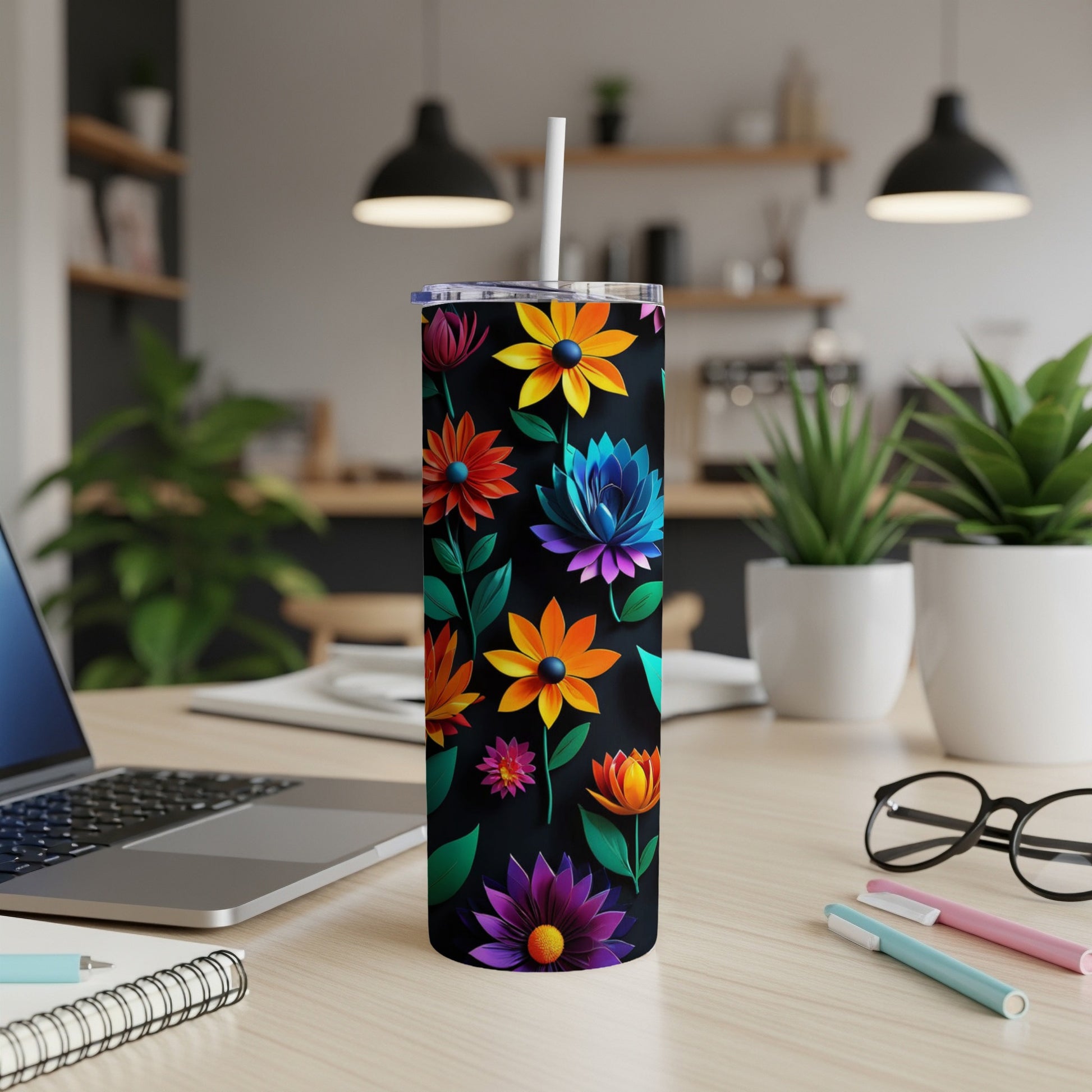 Black tumbler with colorful floral pattern, straw, on a desk.