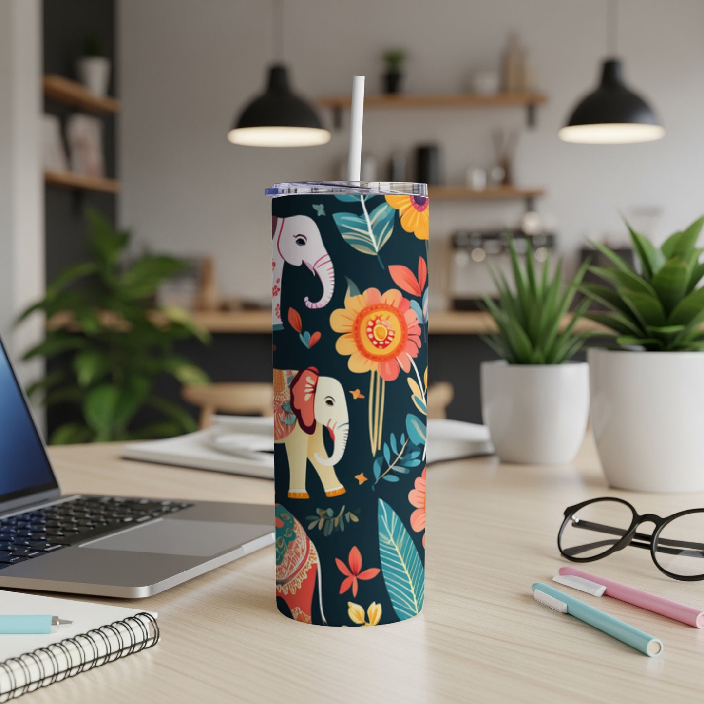 Floral pattern tumbler with elephants and a straw on a desk.