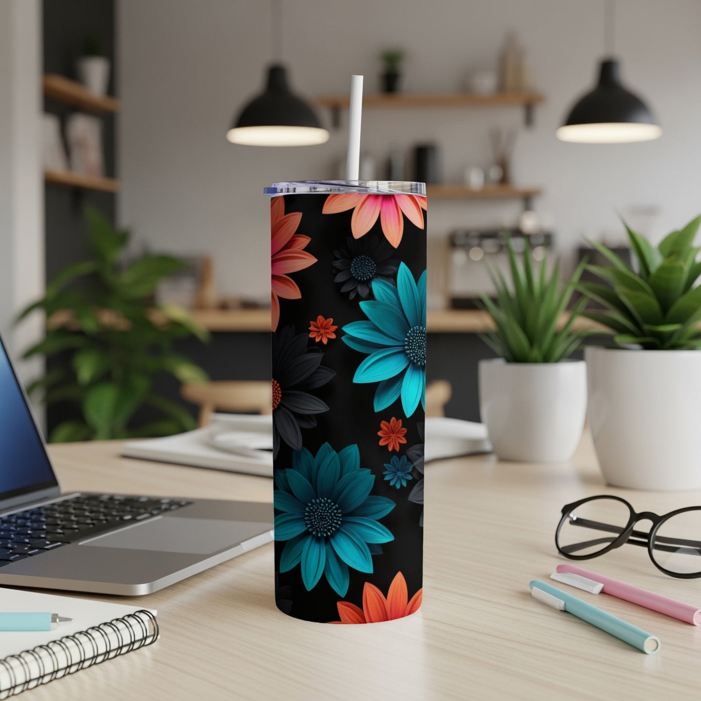 Black tumbler with colorful floral pattern, straw, and pens on desk.