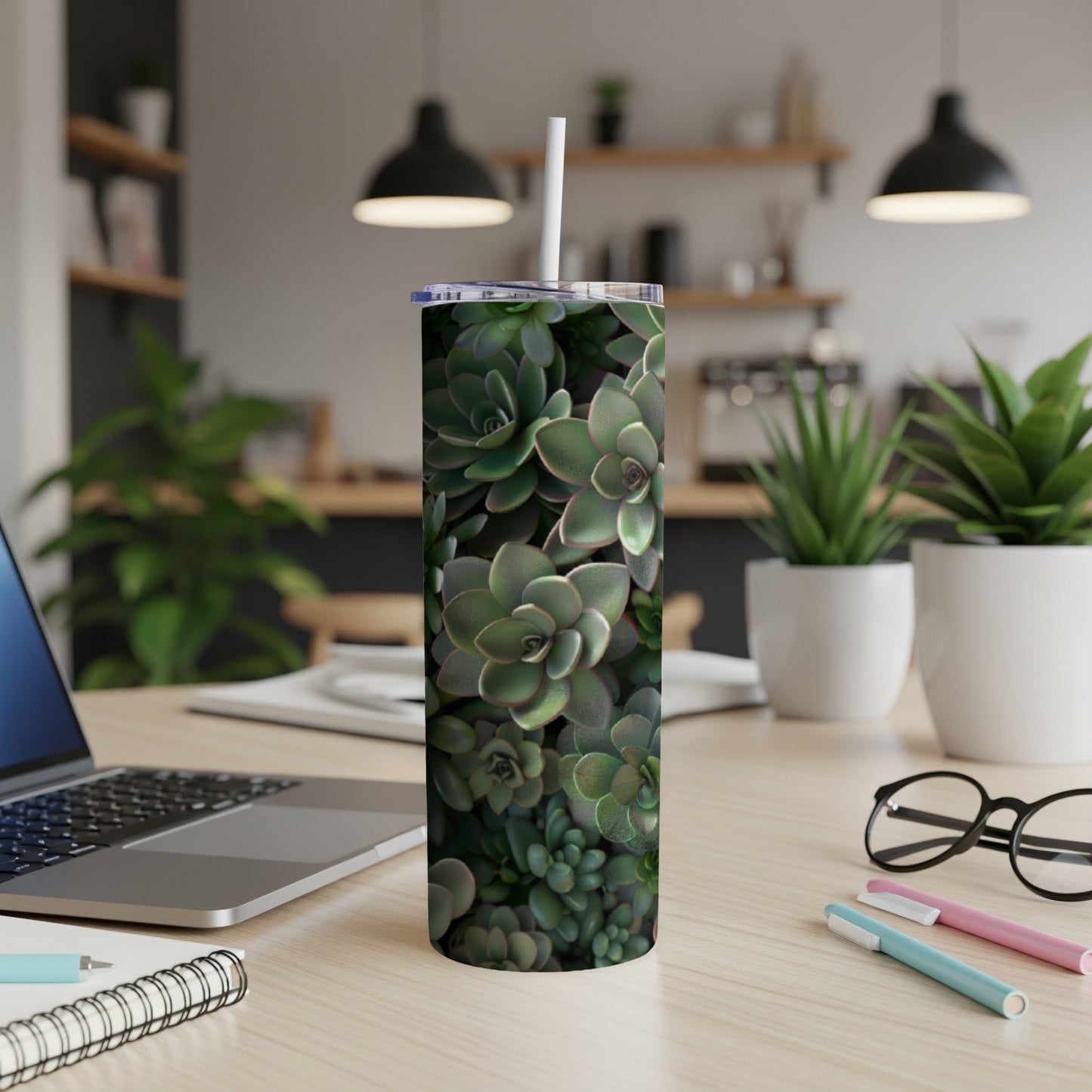 Green succulents fill a tumbler on a desk with a laptop and pens.