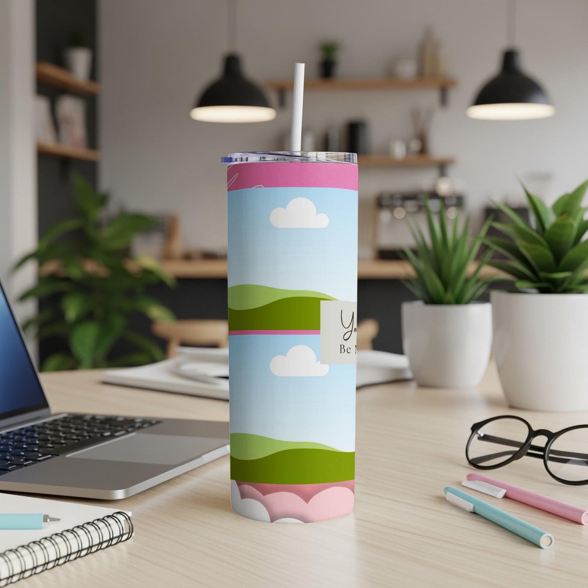 Tumbler with clouds, rolling hills, and text "You Be M" on a desk.