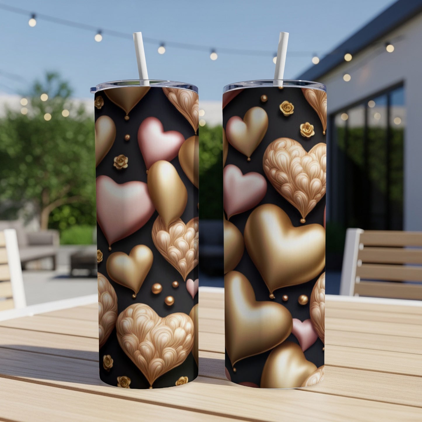 Two gold and pink heart-patterned tumblers with straws on a wooden table.