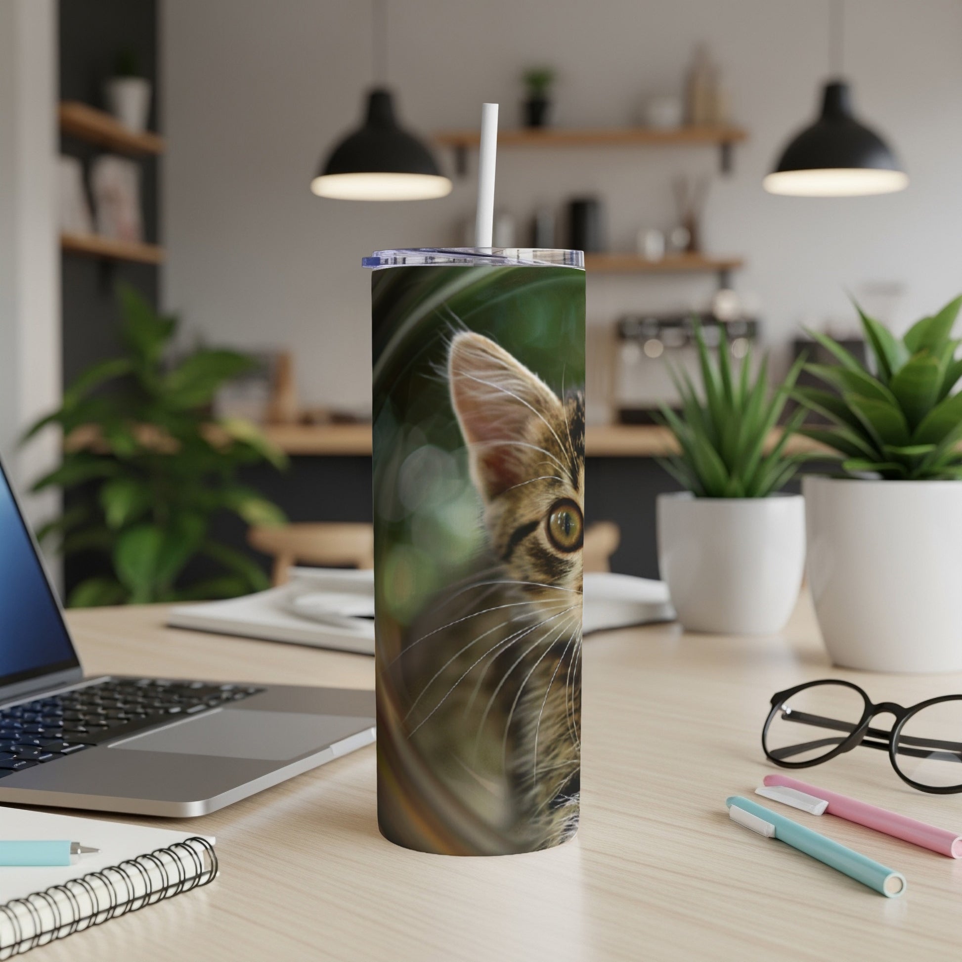Close-up of a tabby kitten's face on a patterned tumbler with a straw.