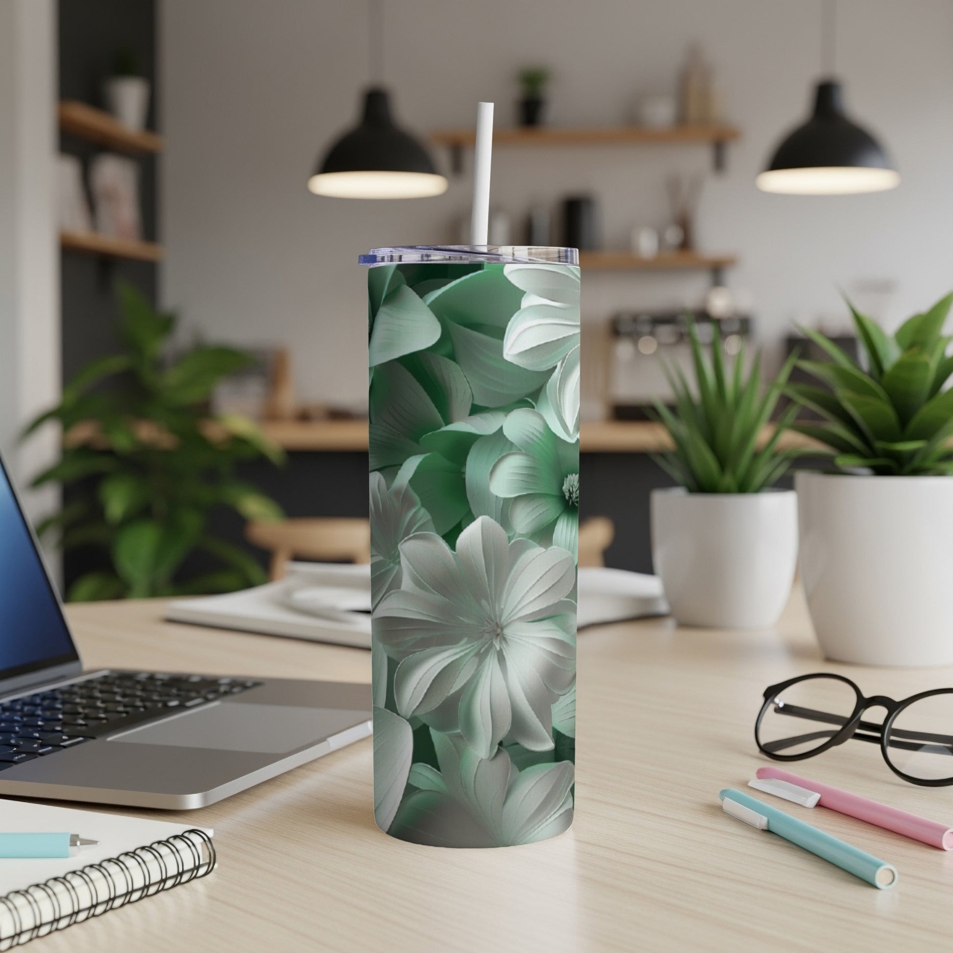 Green floral tumbler with straw on a desk with laptop and pens.