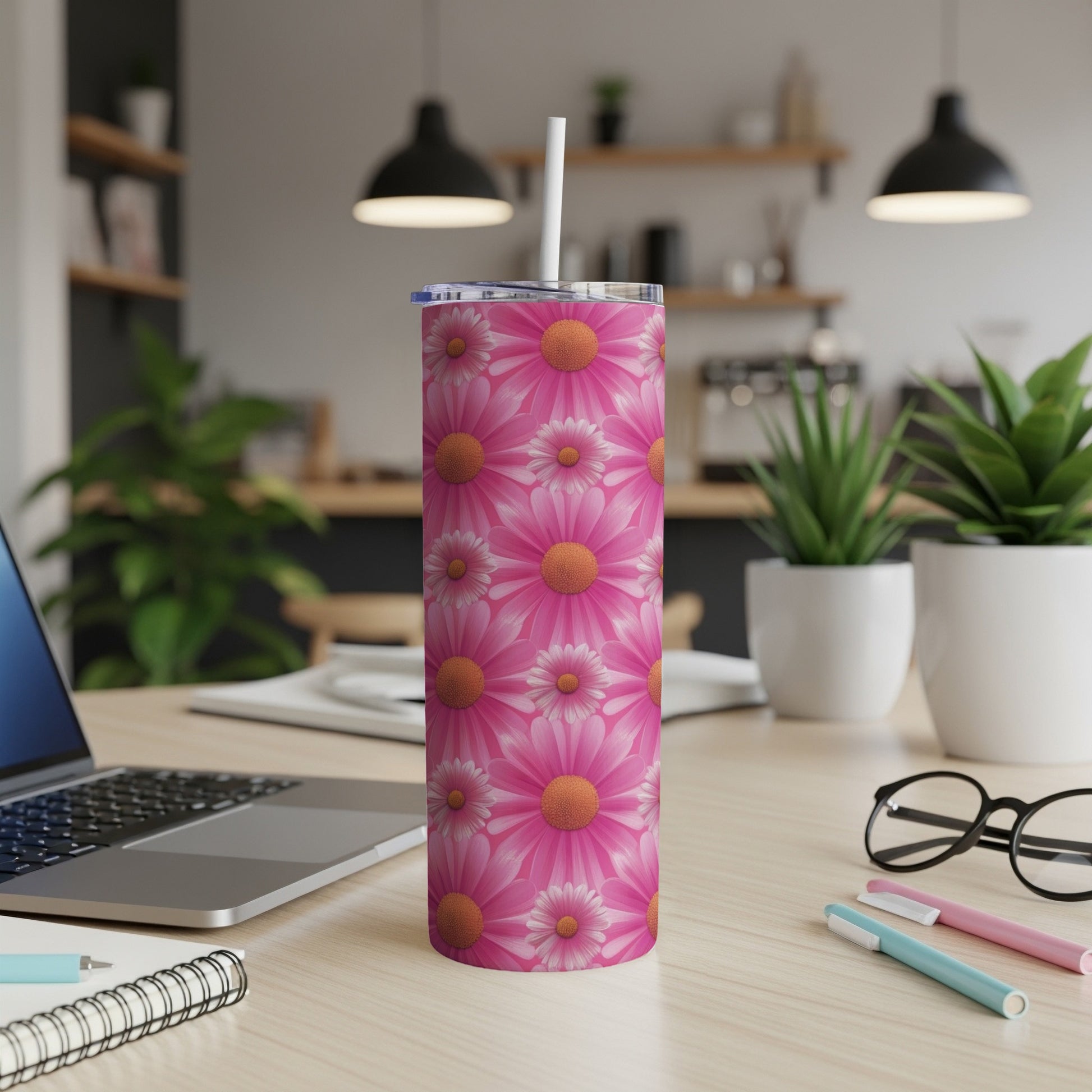 Pink floral tumbler with a straw on a desk with a laptop and pens.