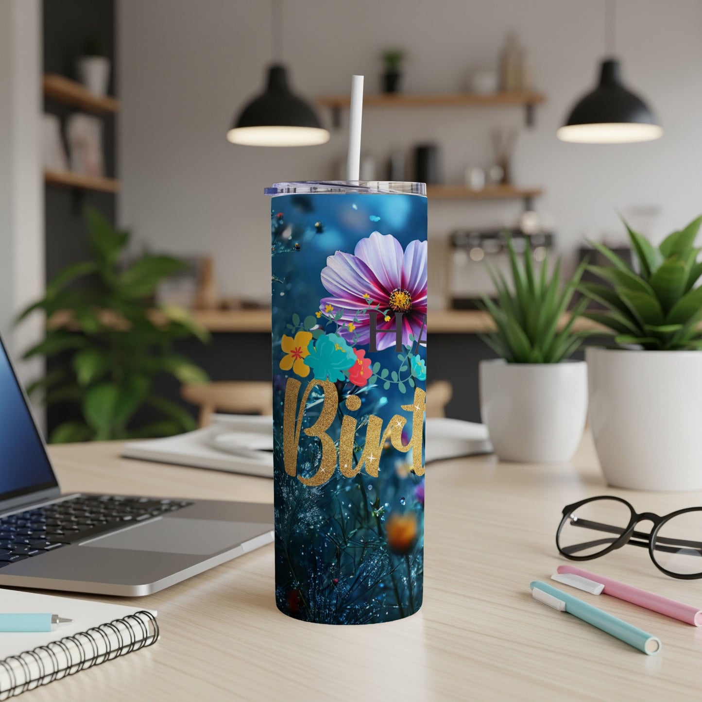 Gold text "Birthday" on a floral skinny tumbler with straw on a desk.