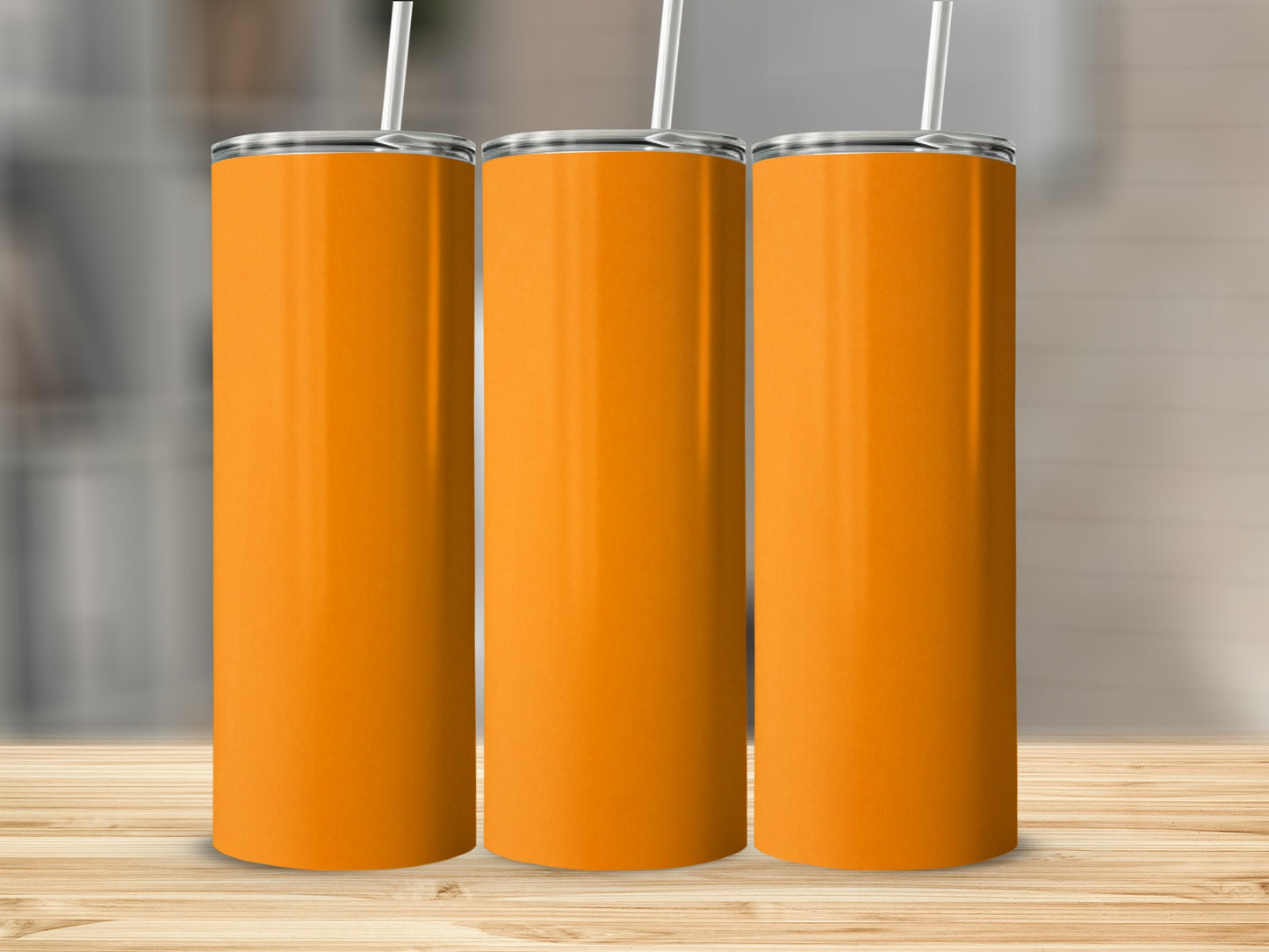 Three blank orange tumblers with straws on a wooden surface.