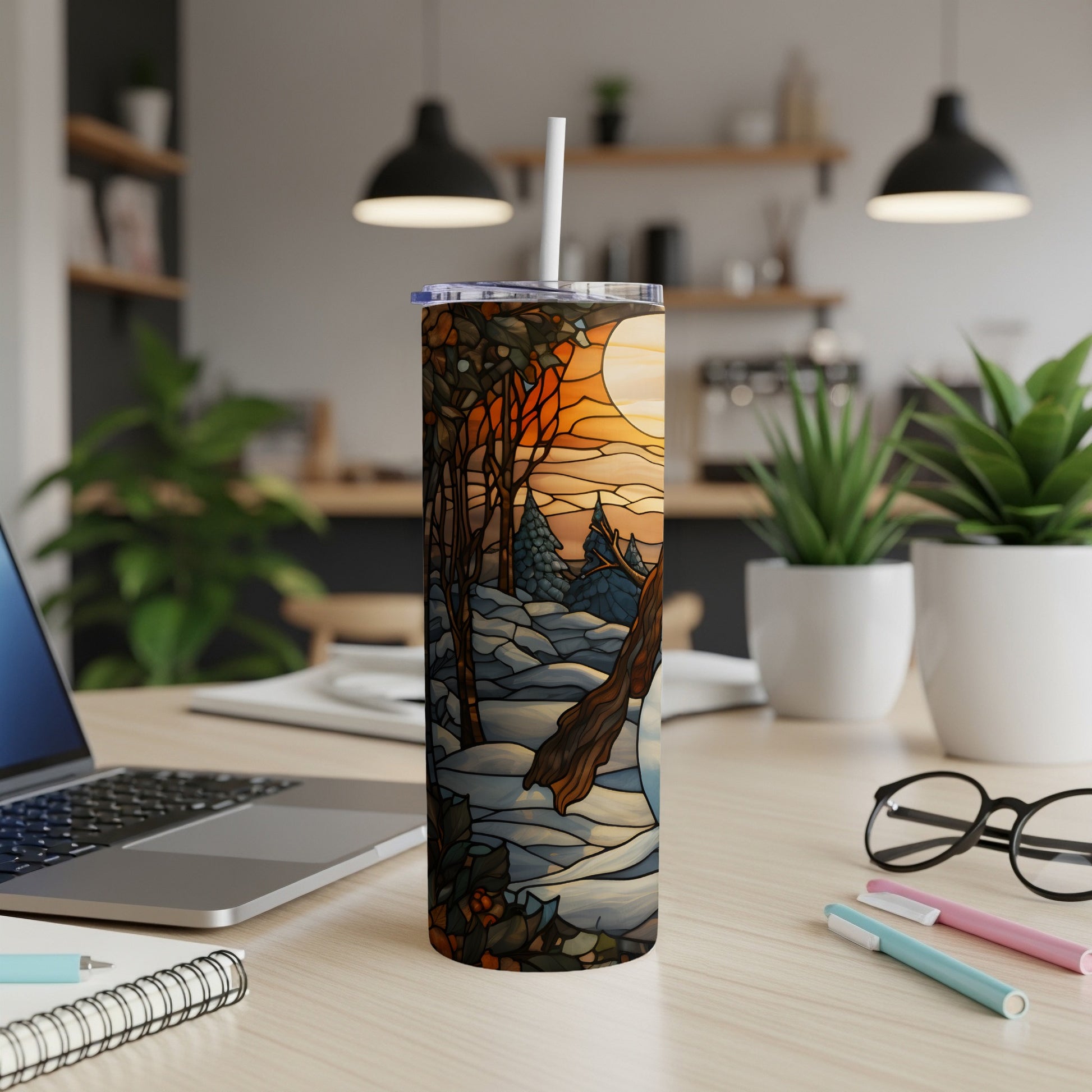 Stained glass winter scene tumbler with straw on desk.
