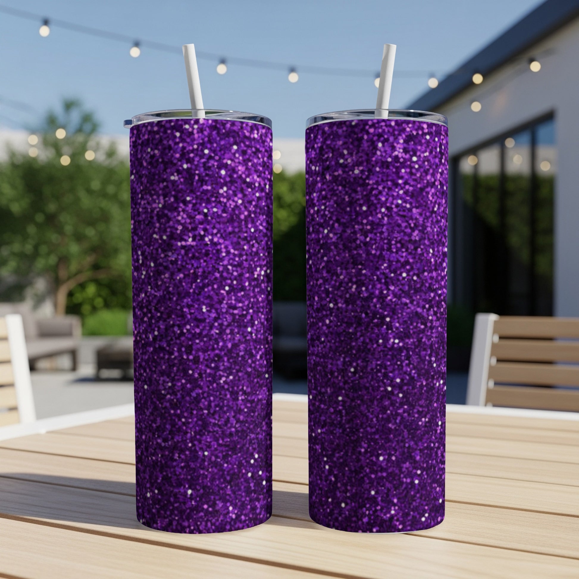 Two tall purple glitter tumblers with straws on a wooden table outdoors.