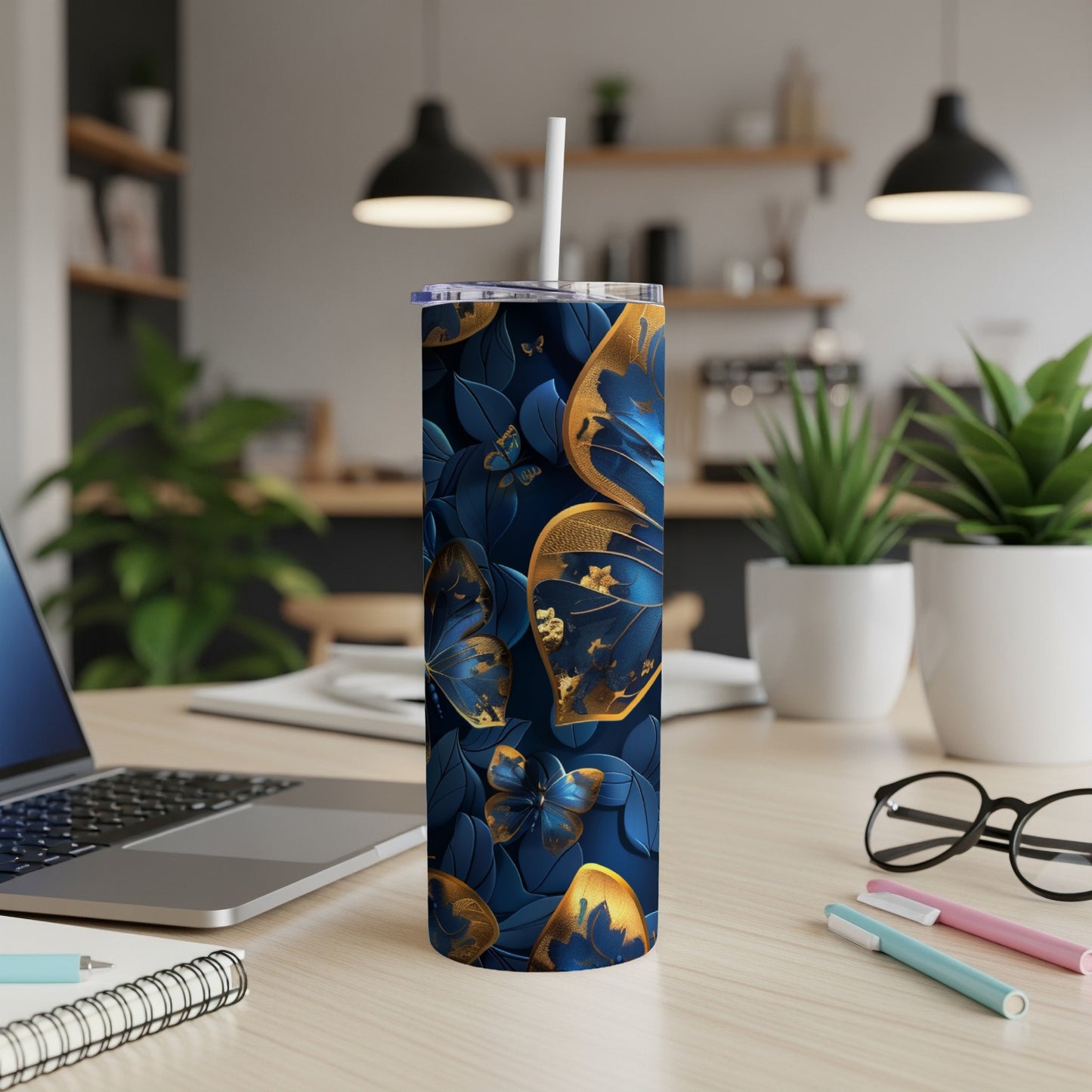 Blue and gold butterfly tumbler with a straw on a wooden desk.