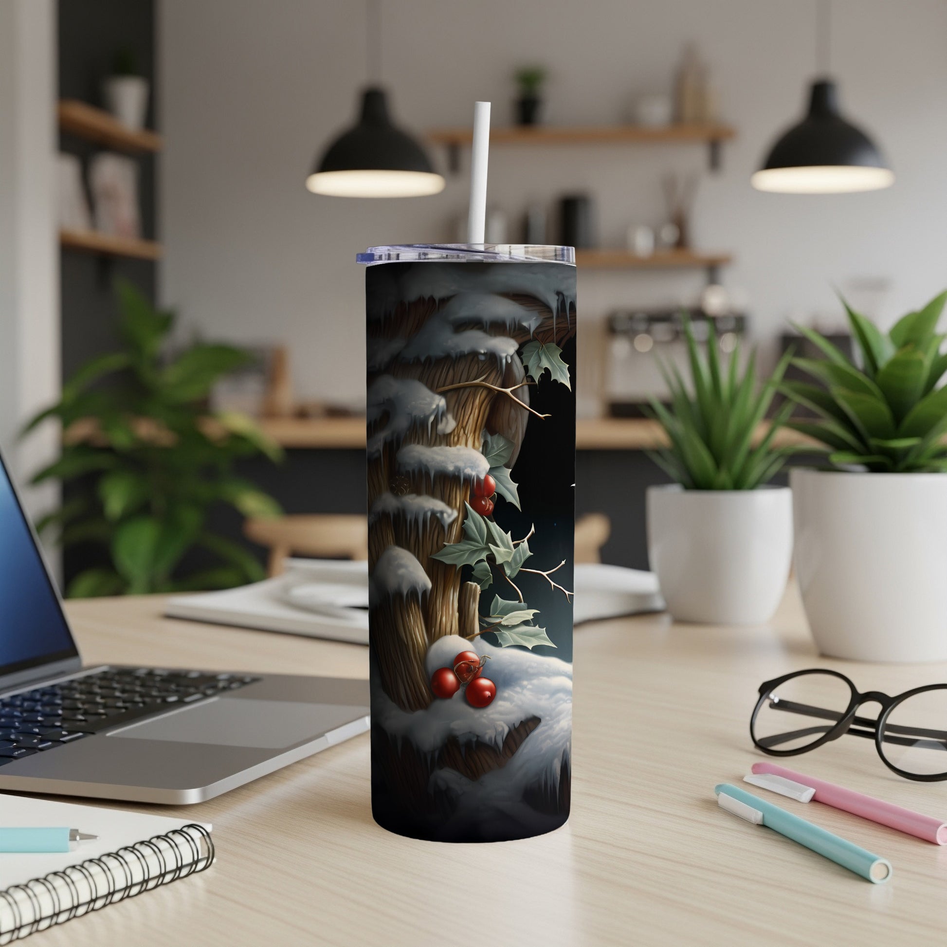 Winter scene tumbler with snow-covered branches and holly on a desk.
